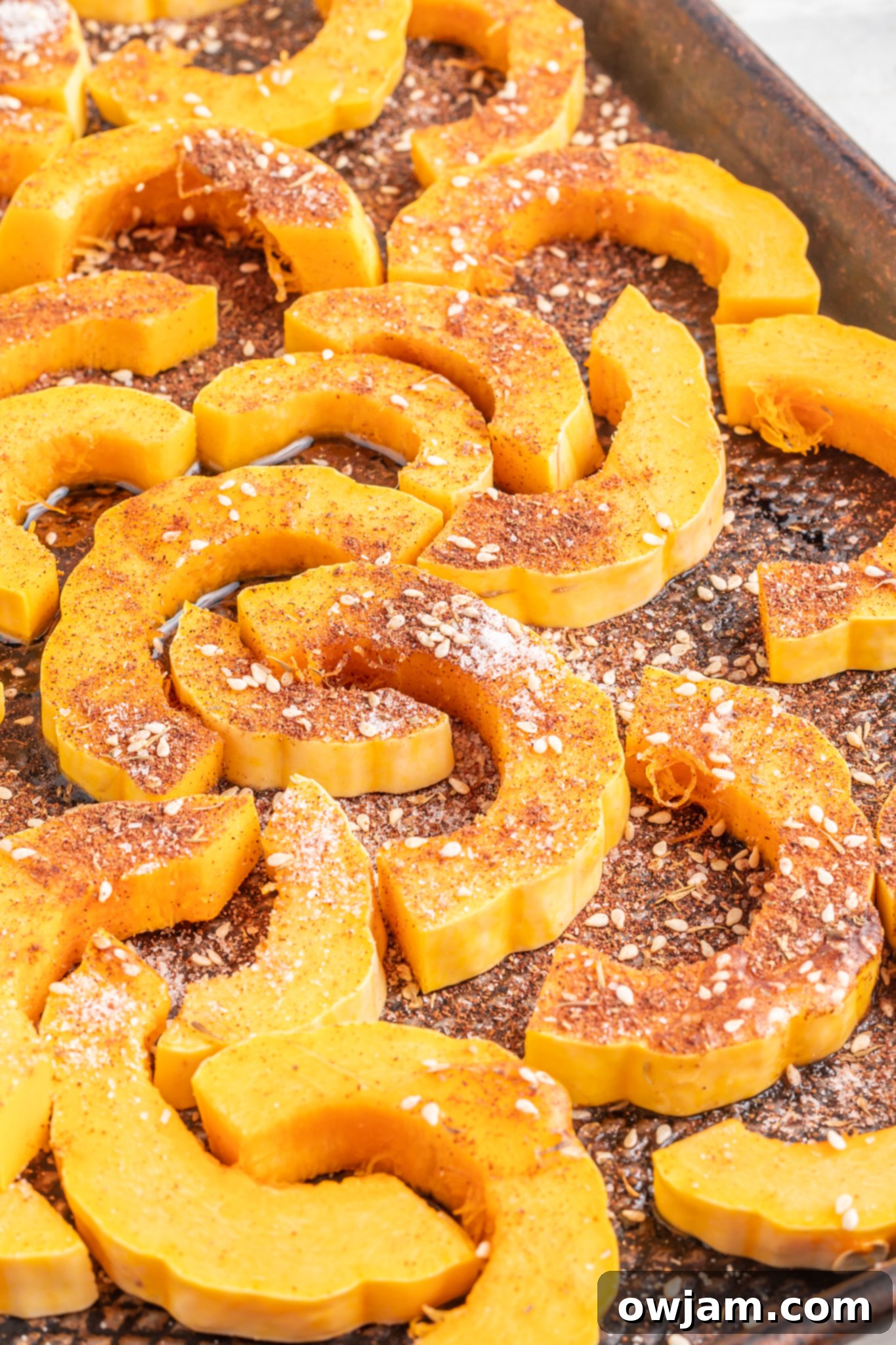 Close-up of delicata squash slices seasoned with za'atar on a baking sheet, ready for roasting.