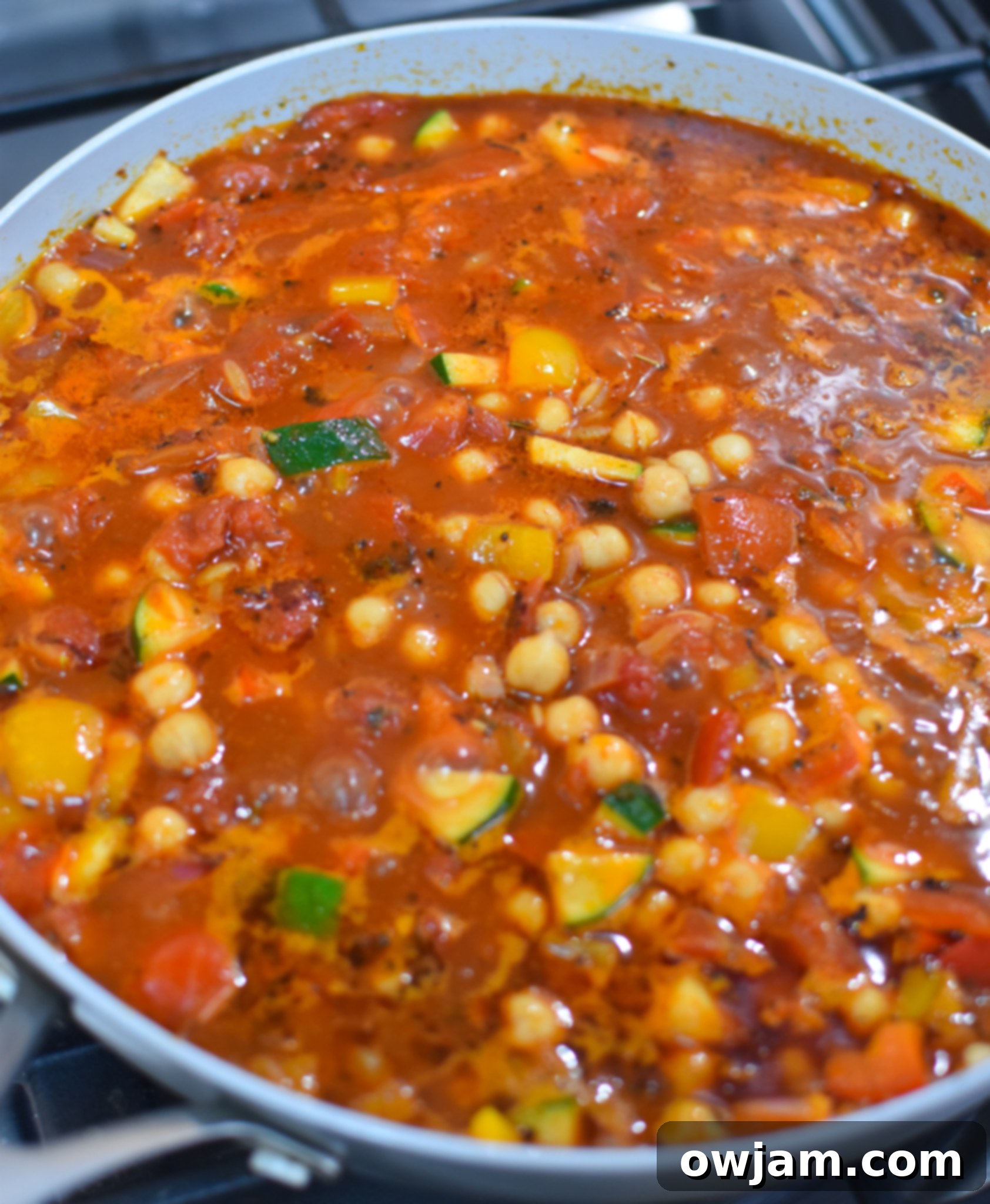 Mediterranean Orzo Pasta simmering in a skillet with broth and vegetables.