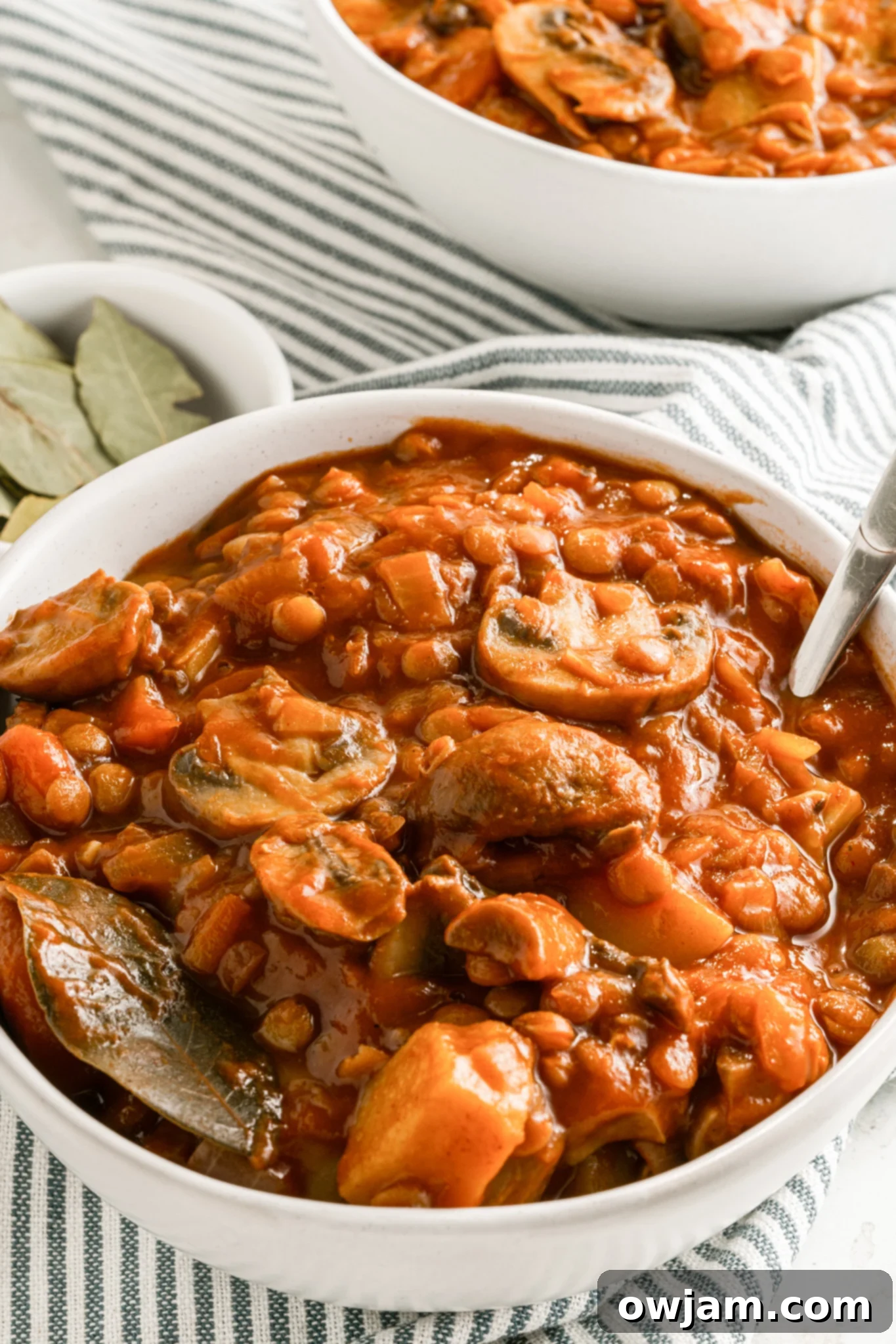 A bowl of hot Lentil Mushroom Stew, served with a spoon and garnished with fresh herbs.