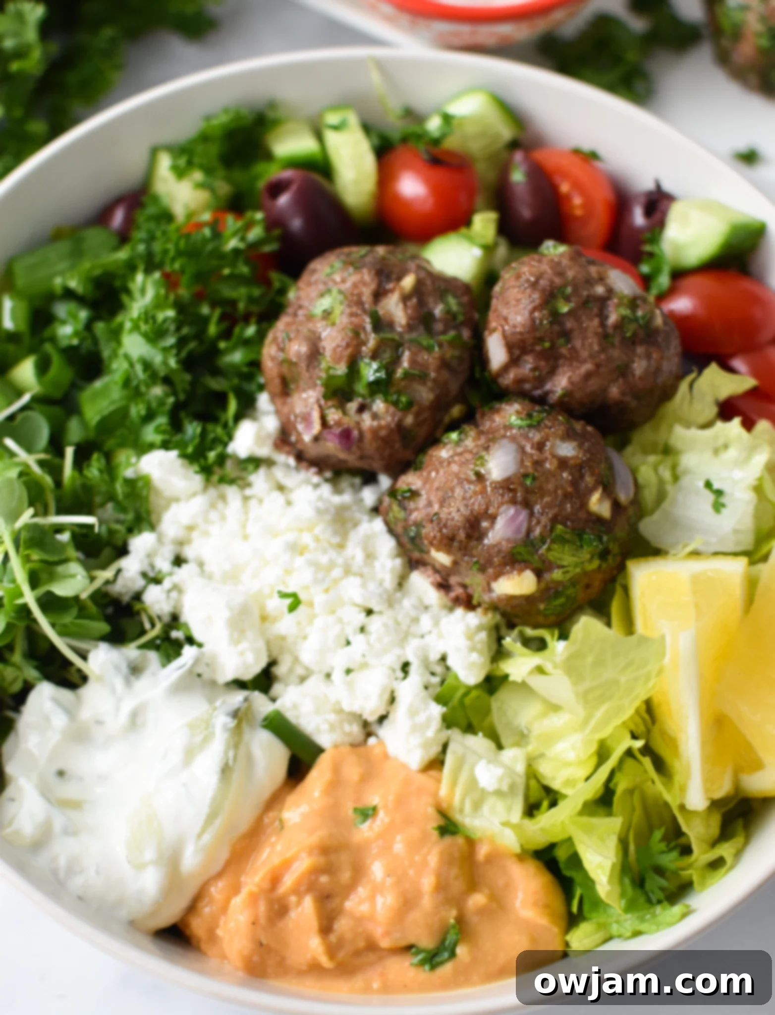Mediterranean Baked Beef Meatballs in a hummus bowl.