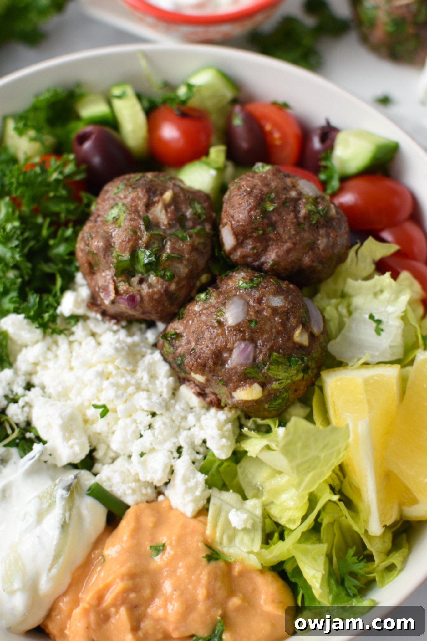 Mediterranean Baked Beef Meatballs in a hummus bowl.