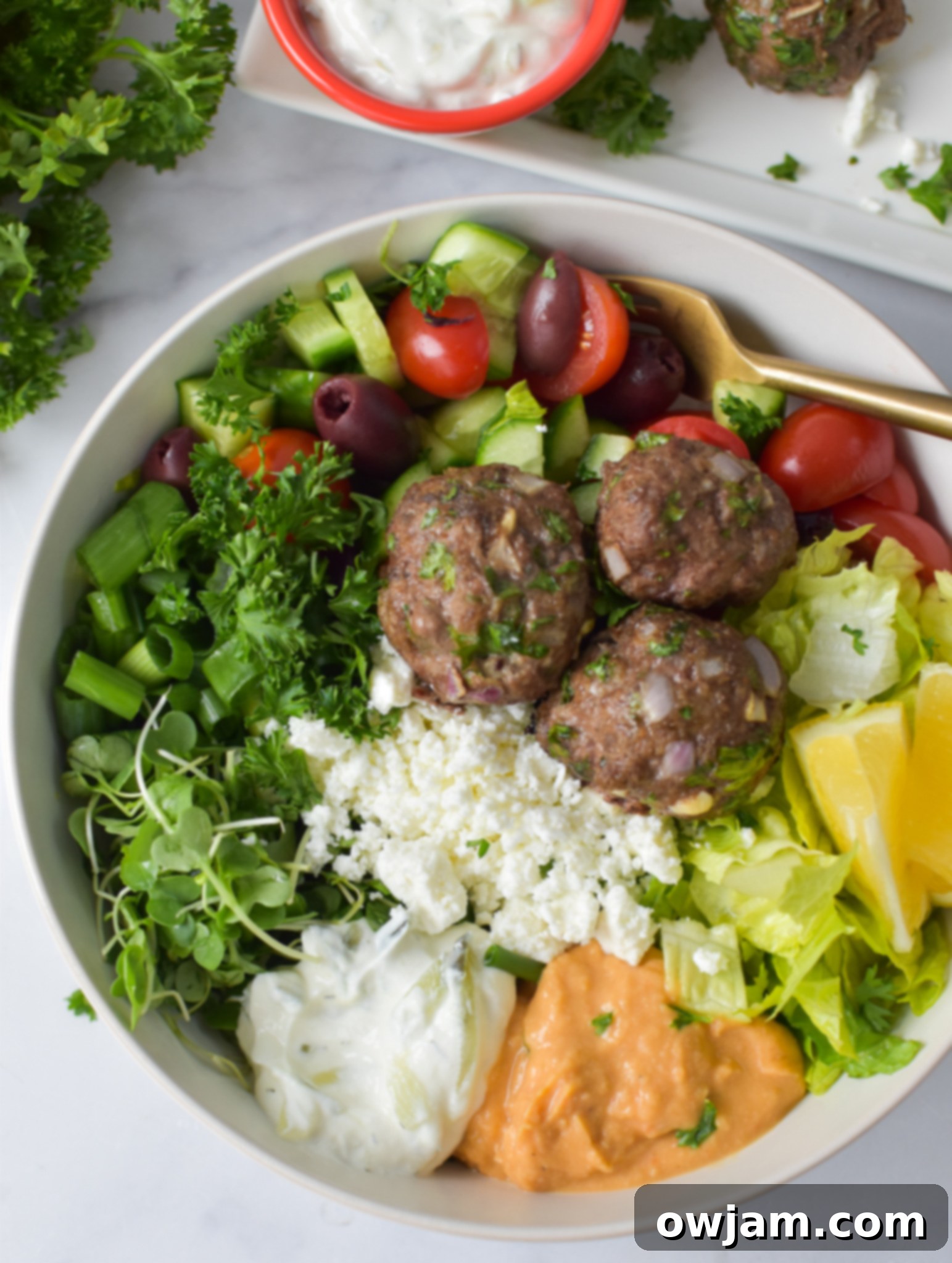 Mediterranean Baked Beef Meatballs in a hummus bowl with vegetables.