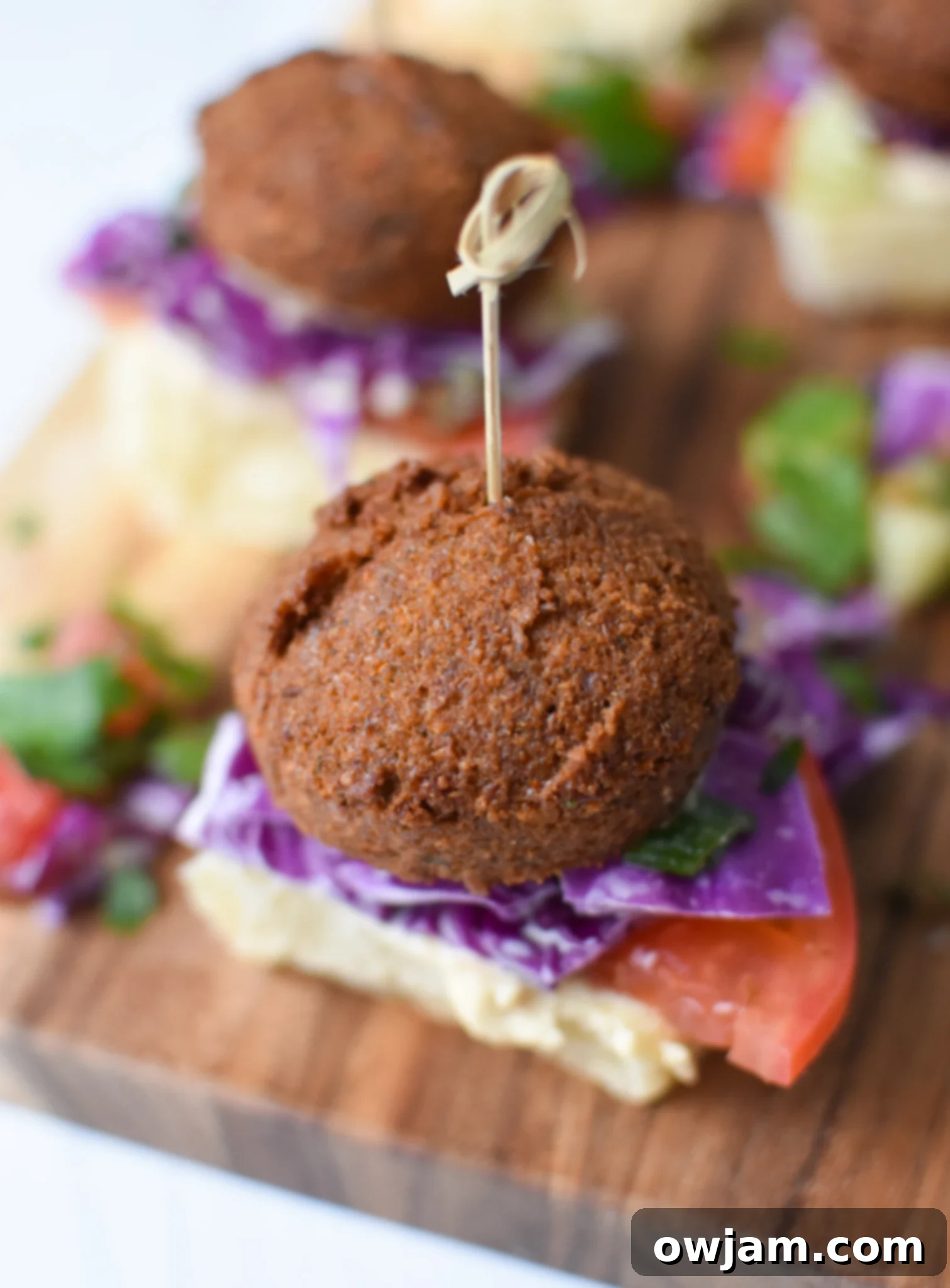 Falafel Sliders with Tangy Tahini Slaw 2 Falafel Sliders with Tahini Slaw with toothpick in the slider. A beautifully assembled falafel slider stands tall with a toothpick, showcasing layers of falafel, tahini slaw, tomato, and greens on a slider bun.