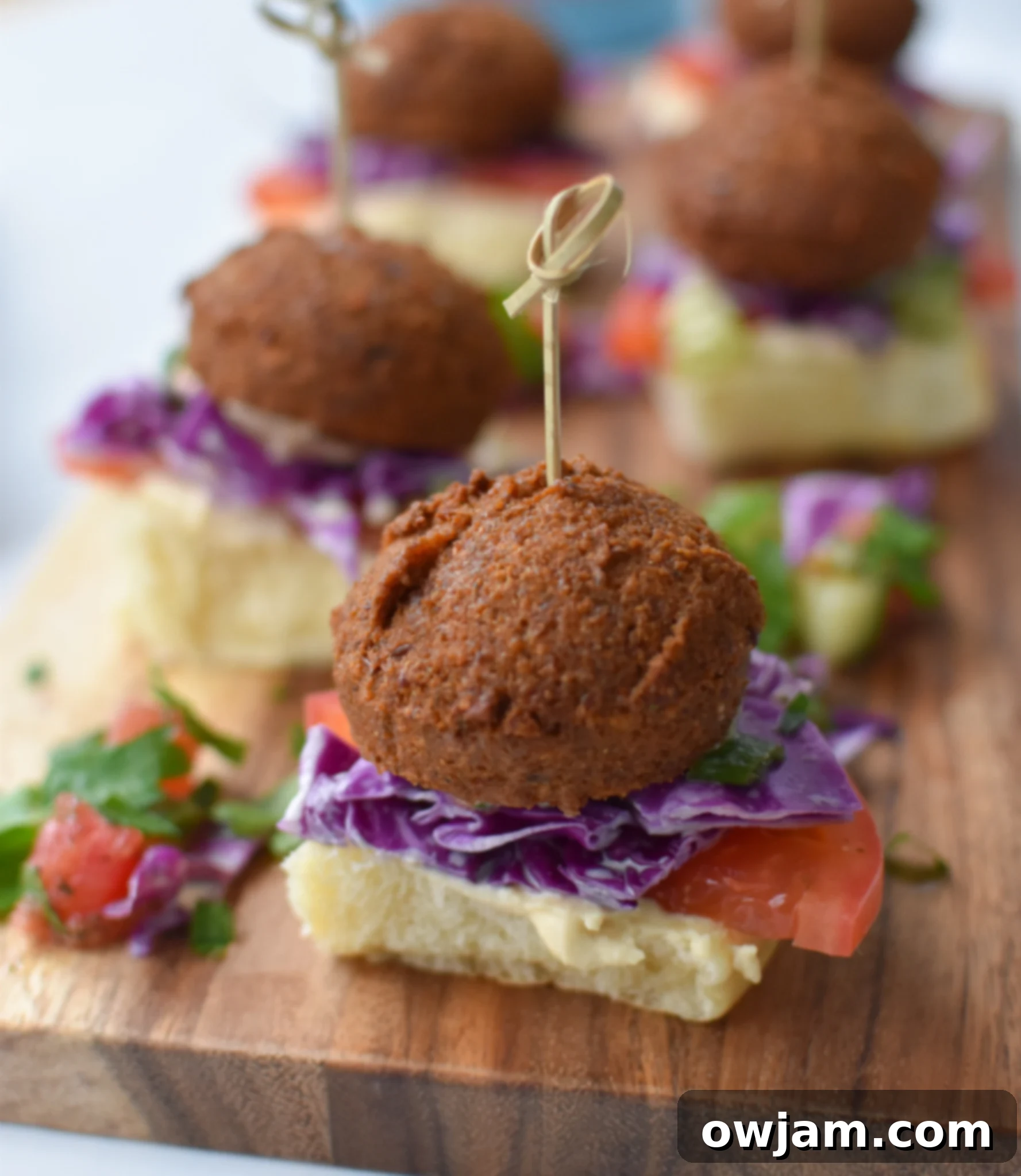 Falafel Sliders with Tangy Tahini Slaw 3 Falafel Sliders with Tahini Slaw on a cutting board. Several assembled falafel sliders are arranged on a rustic wooden cutting board, ready to be served.