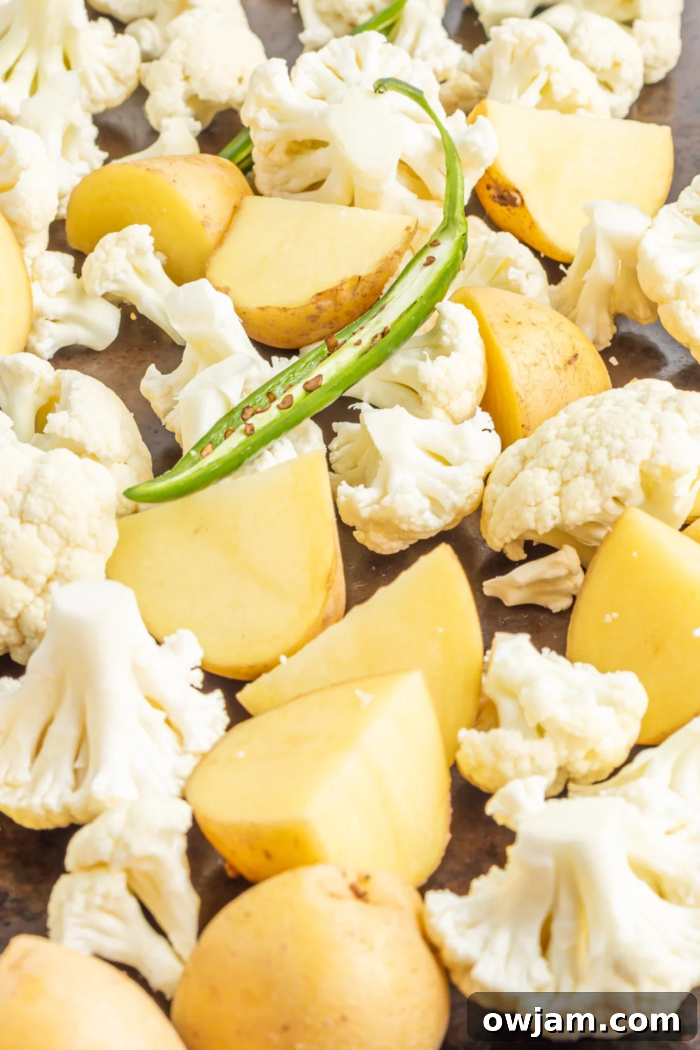 Golden Cauliflower Curry 5 Cauliflower florets and cubed baby potatoes roasting on a baking sheet, lightly seasoned with oil and salt.