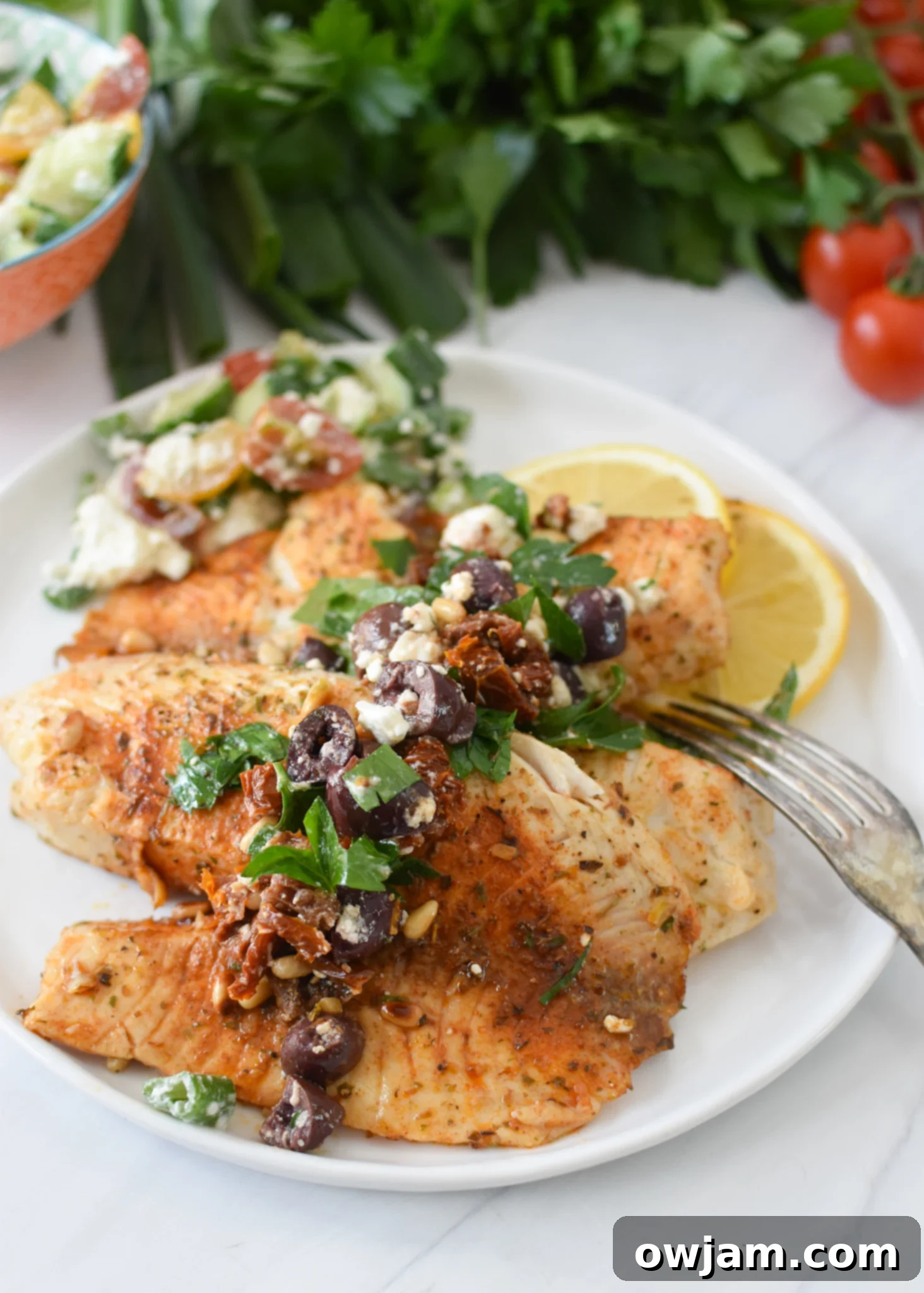 Greek Baked Tilapia with a fork on a white plate.