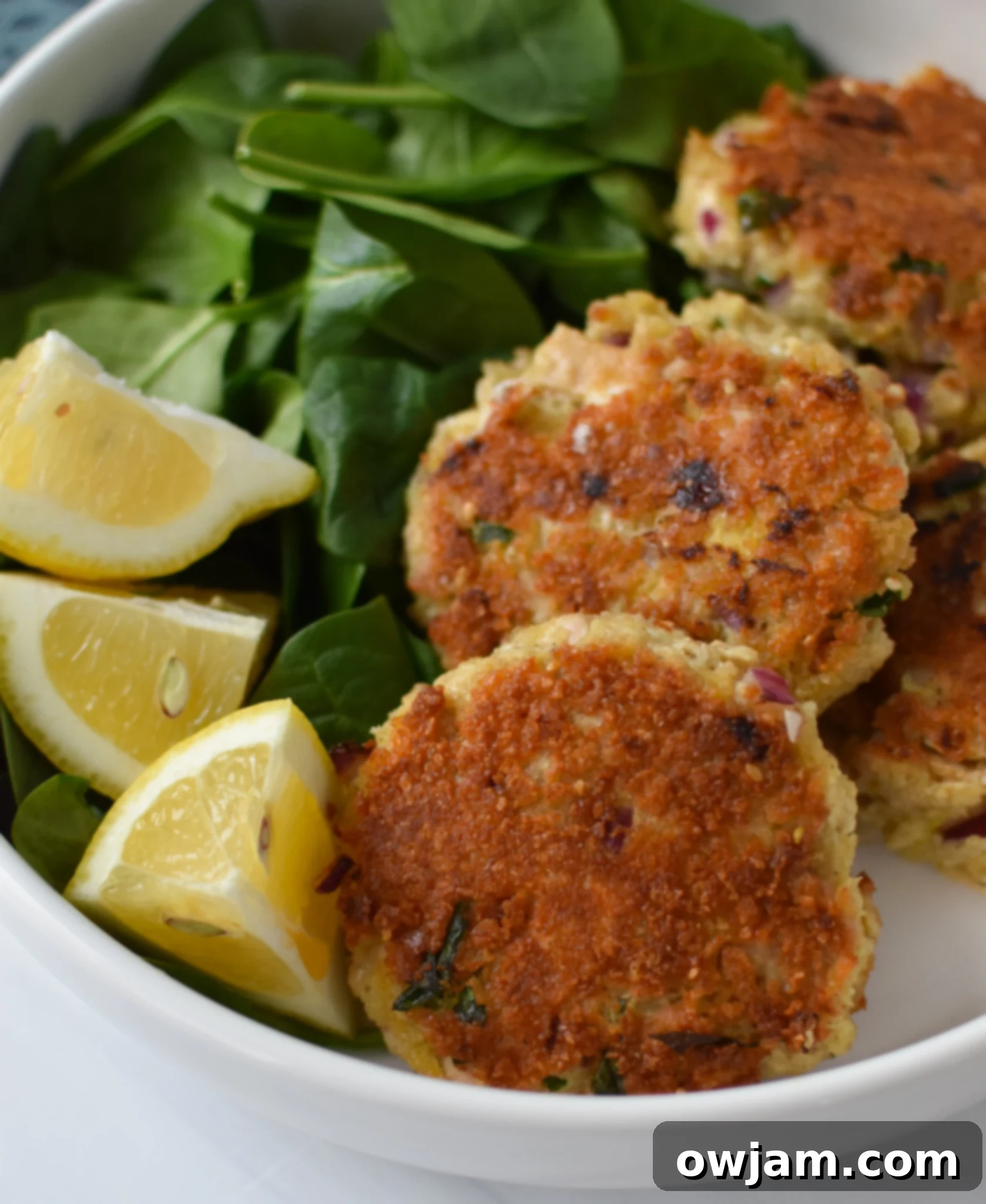 Mediterranean Tuna Patties Recipe in a white bowl, garnished with fresh herbs and lemon wedges.
