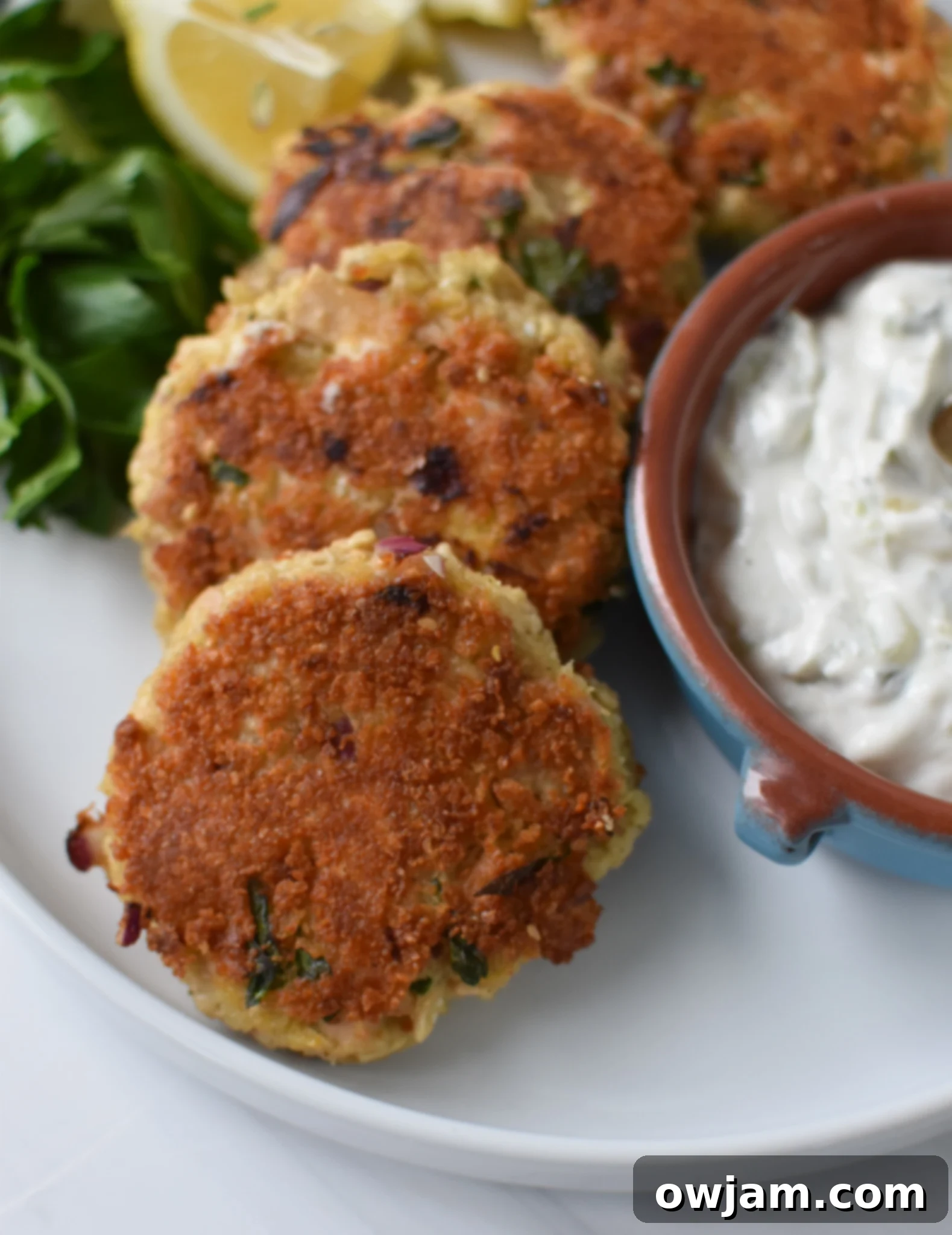 Crispy Mediterranean Tuna Patties served on a white plate with a side of tzatziki sauce and fresh parsley.
