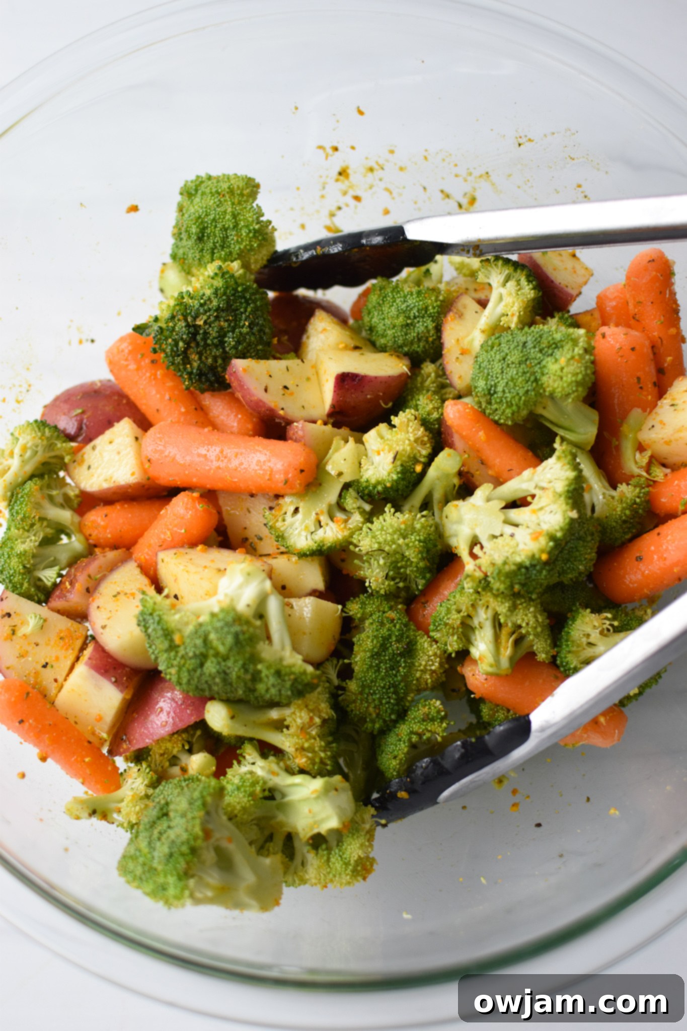 One-Pan Lemon Parmesan Chicken Tenders 6 Vegetables and potatoes coated in seasoning and olive oil in a mixing bowl.