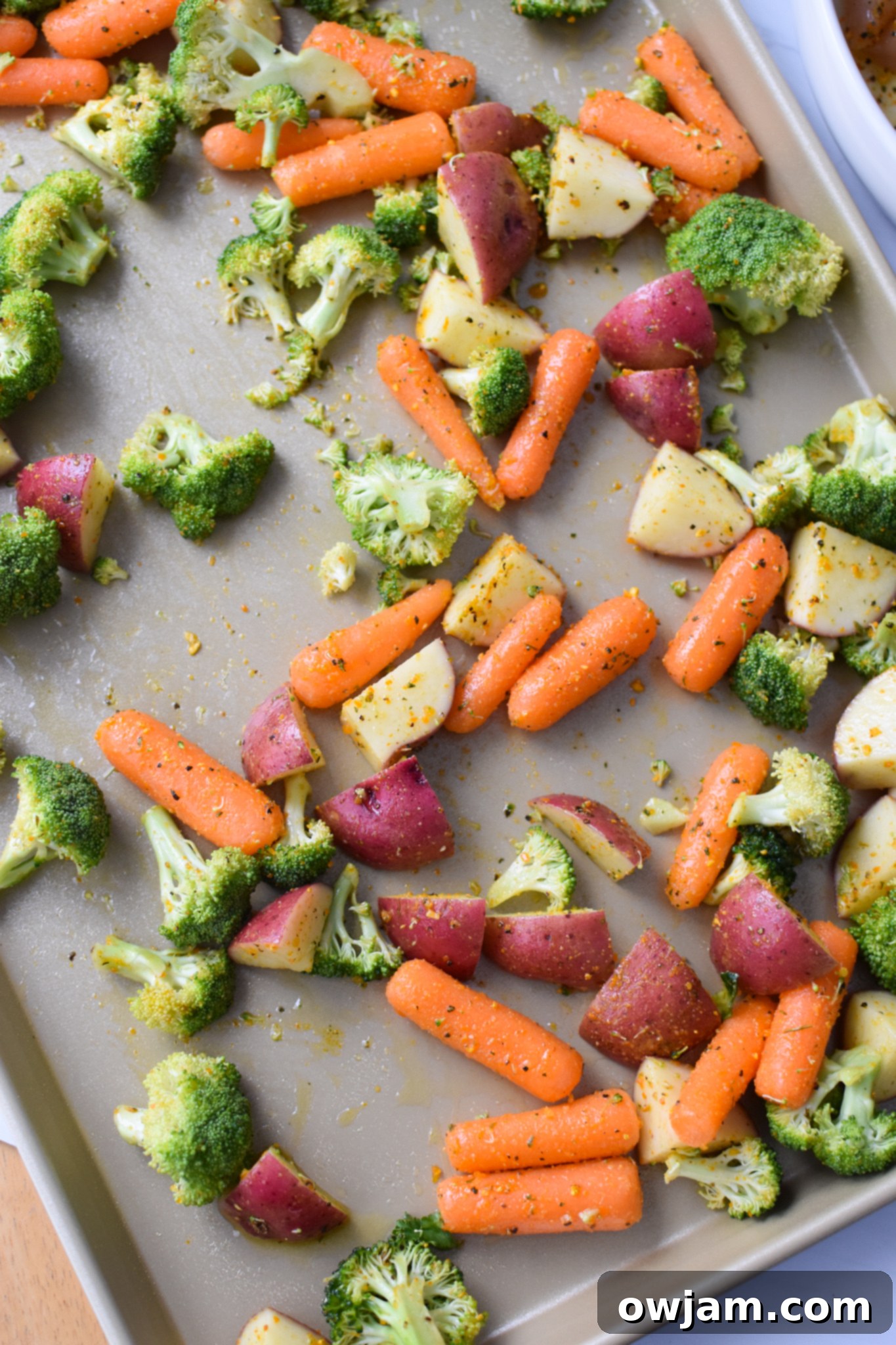 One-Pan Lemon Parmesan Chicken Tenders 7 Seasoned vegetables, including potatoes, carrots, and broccoli, spread in a single layer on a baking sheet.