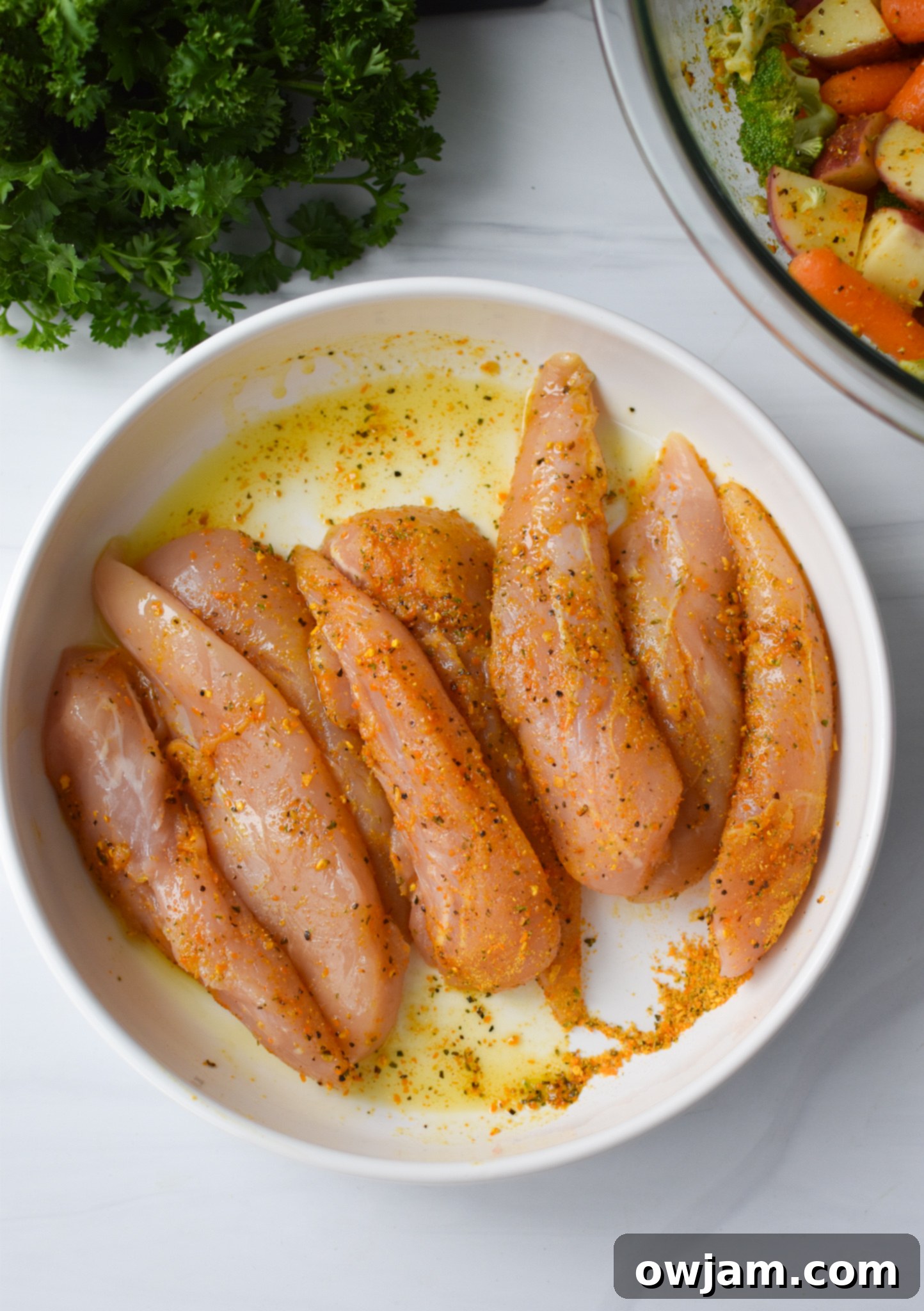 One-Pan Lemon Parmesan Chicken Tenders 8 Raw chicken tenderloins coated in lemon parmesan seasoning and olive oil in a mixing bowl.