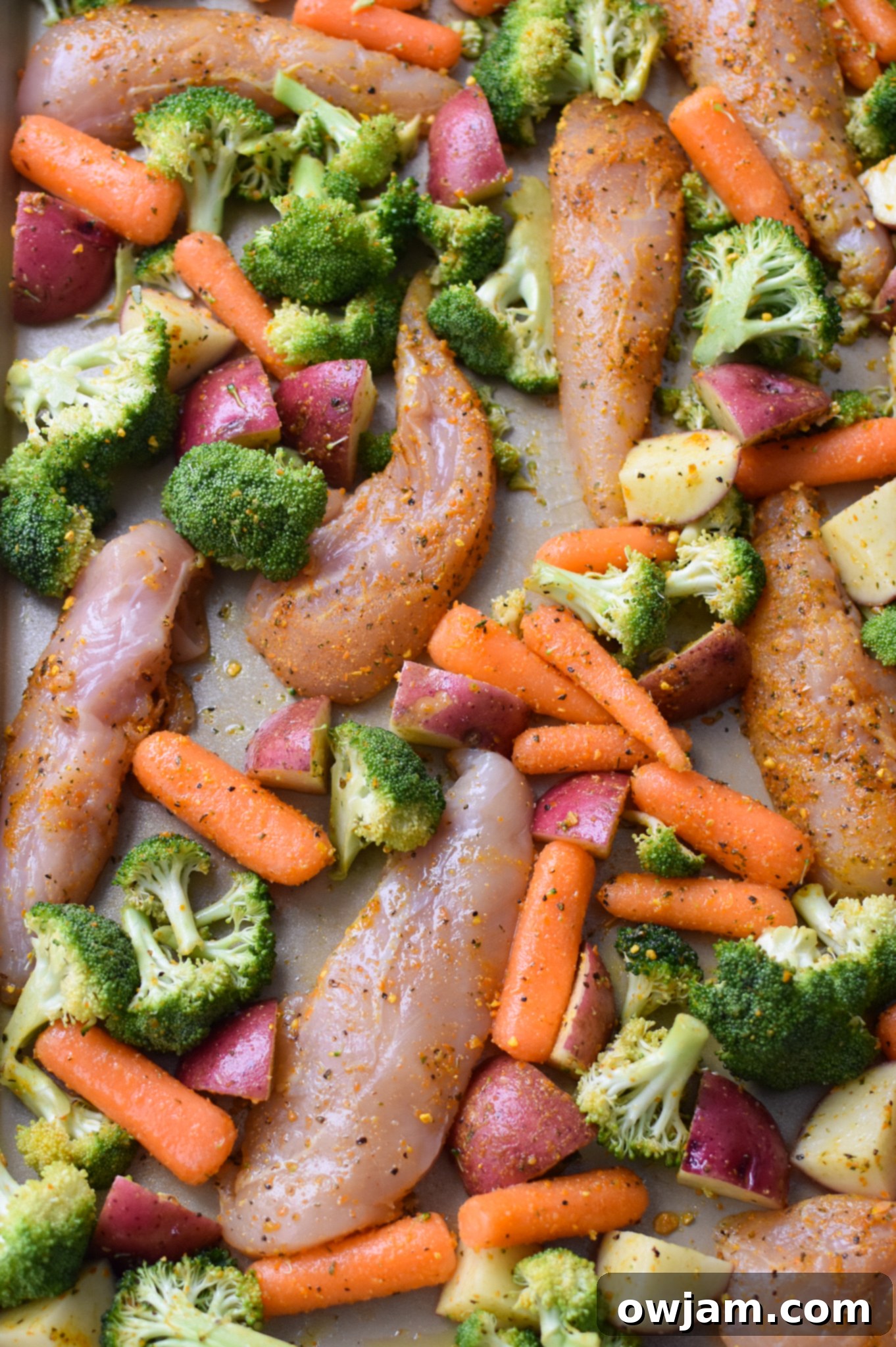 One-Pan Lemon Parmesan Chicken Tenders 9 Uncooked Sheet Pan Lemon Parmesan Chicken Tenders and seasoned vegetables arranged on a single baking sheet, ready for the oven.