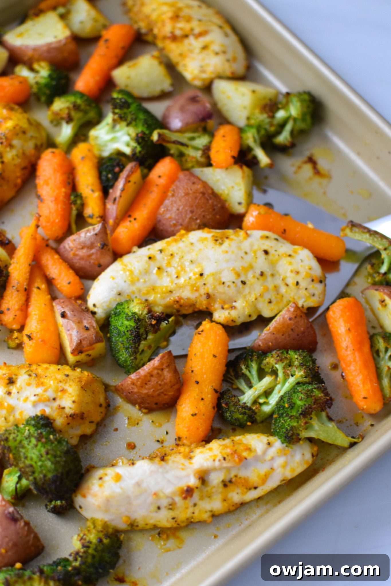 One-Pan Lemon Parmesan Chicken Tenders 10 Finished Sheet Pan Lemon Parmesan Chicken Tenders and roasted vegetables on a baking sheet, with a spatula lifting a portion.