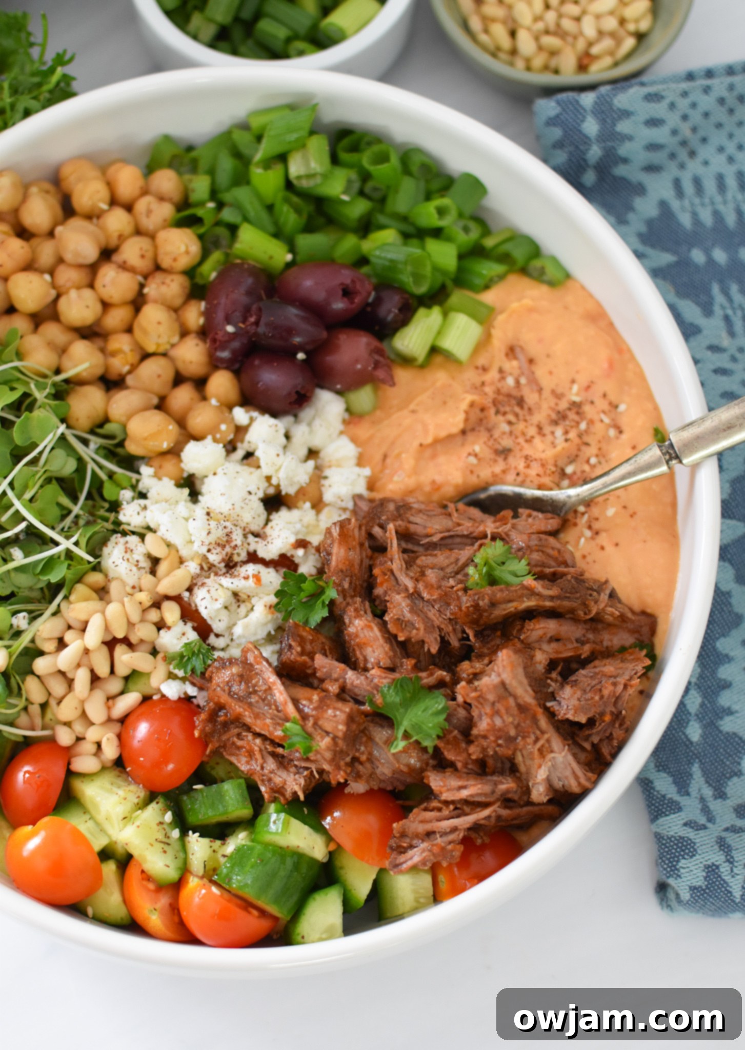 Mediterranean Shredded Beef Hummus Bowls 7 A fork piercing into a Slow Cooker Shredded Beef Hummus Bowl, showcasing the layers of fresh ingredients and tender beef.