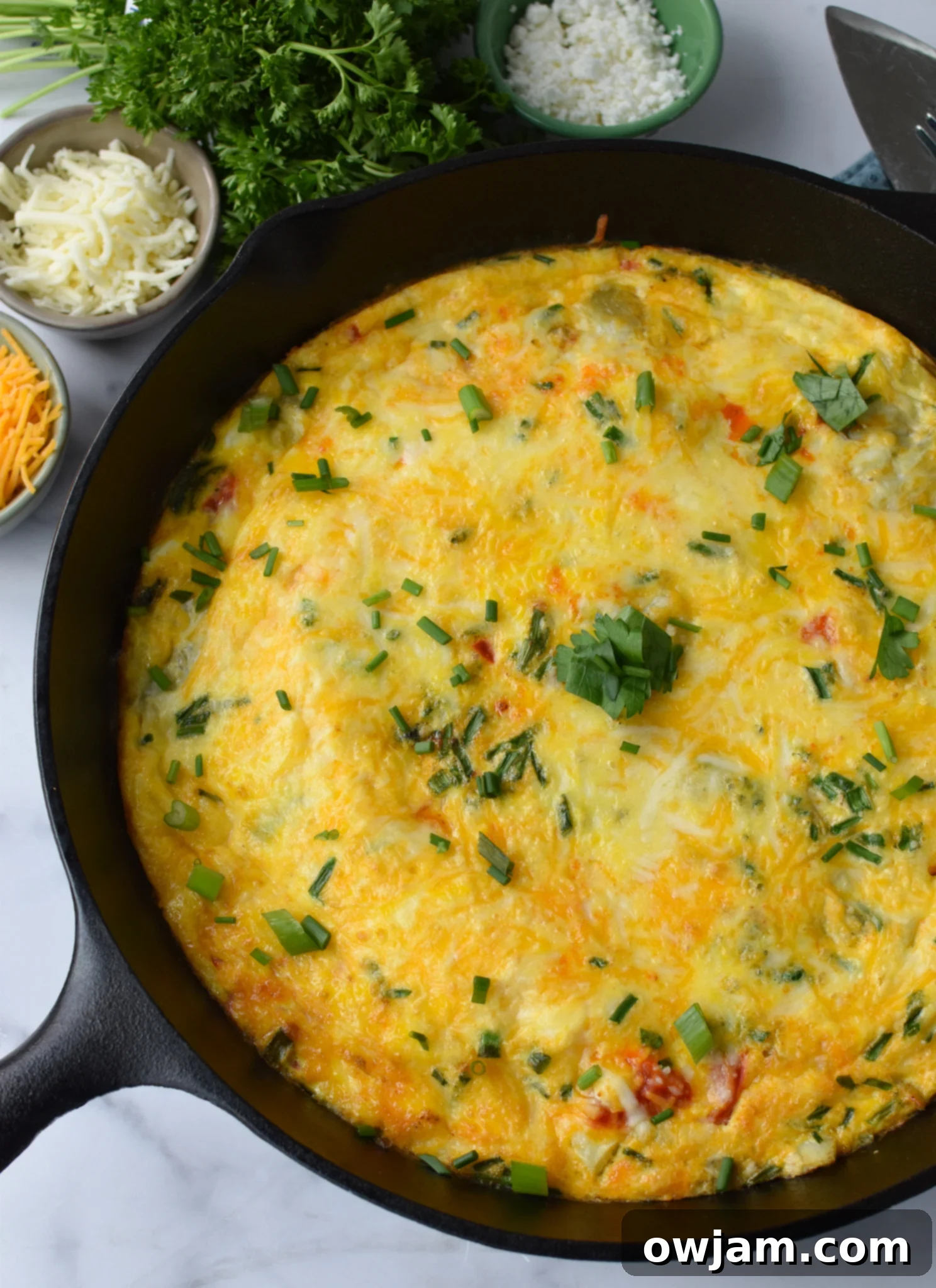 Mediterranean Vegetable Frittata Recipe with fresh chives. A golden-brown frittata topped with fresh green chives, served in a cast iron skillet, ready to be enjoyed for breakfast or brunch.