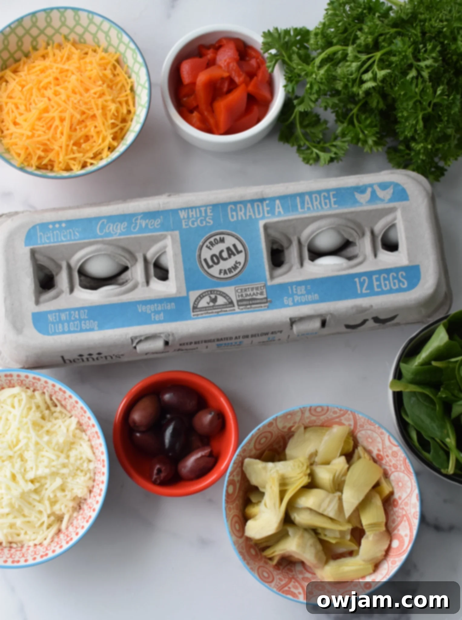 Mediterranean Vegetable Frittata Recipe ingredients. A flat lay photo showing all the fresh ingredients for the frittata: eggs, spinach, red onion, roasted red peppers, feta cheese, mozzarella, cheddar, artichokes, and spices.