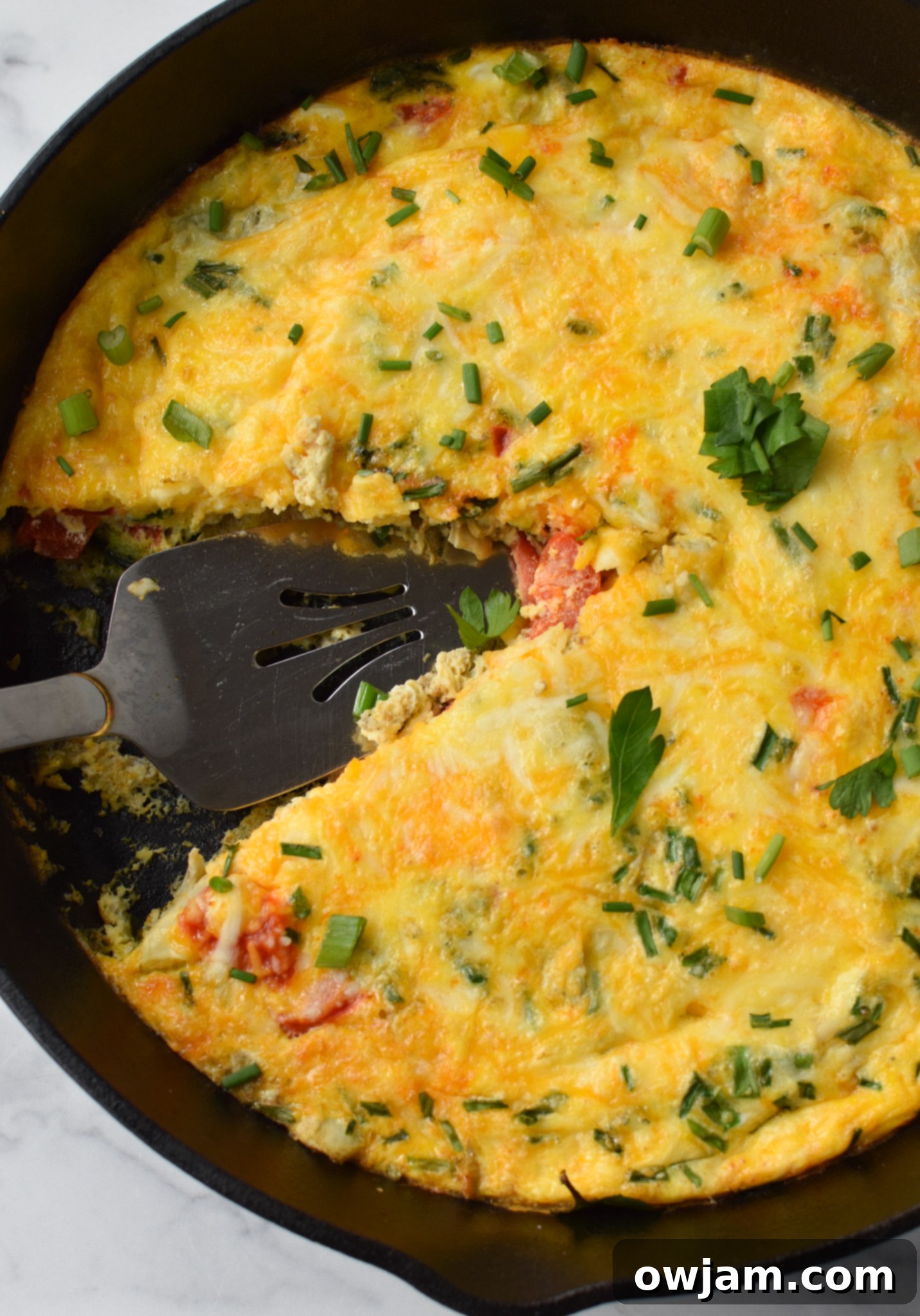 Mediterranean Vegetable Frittata Recipe with a pie cutter. A freshly baked Mediterranean frittata in a cast iron skillet, being perfectly portioned with a pie cutter, ready for serving.