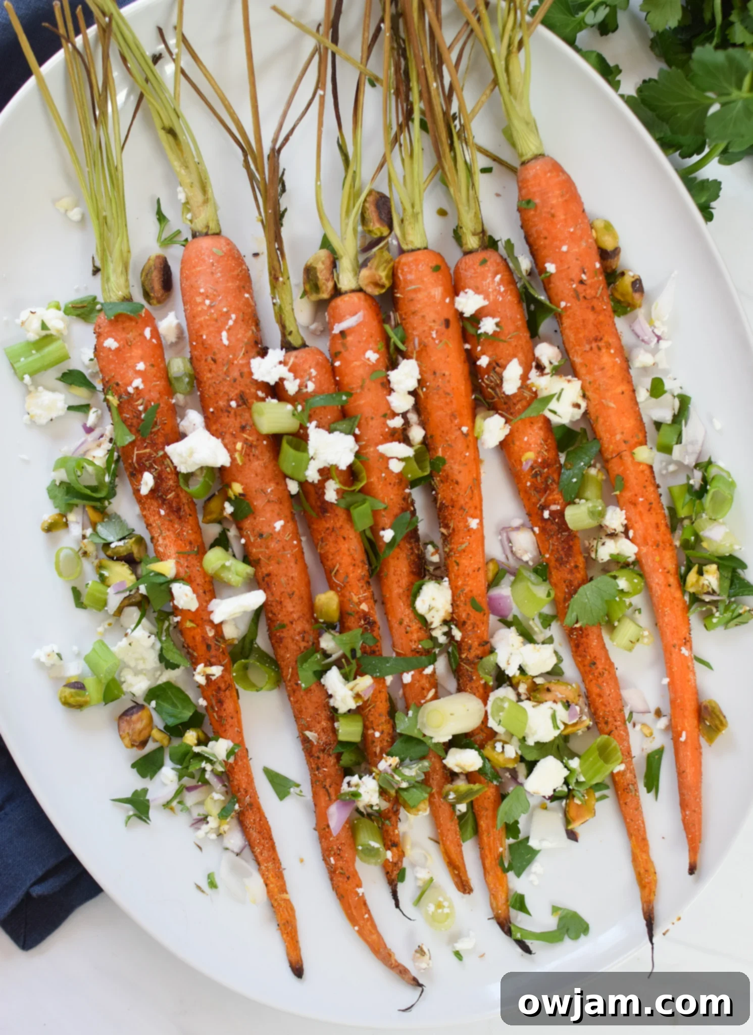 Roasted Carrots with Pistachios on a white platter, garnished with fresh herbs and feta.