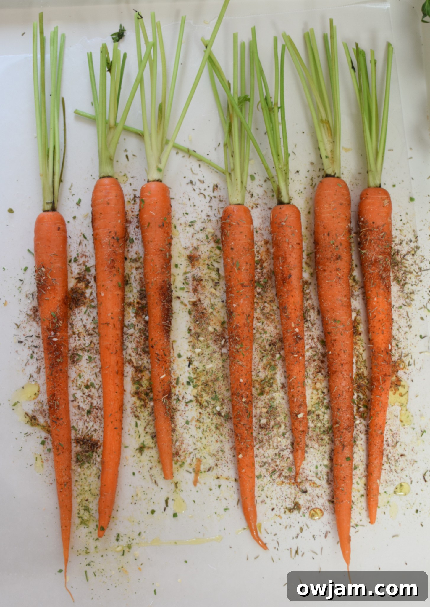 Seasoned carrots with pistachios spread on a baking sheet, ready for roasting.