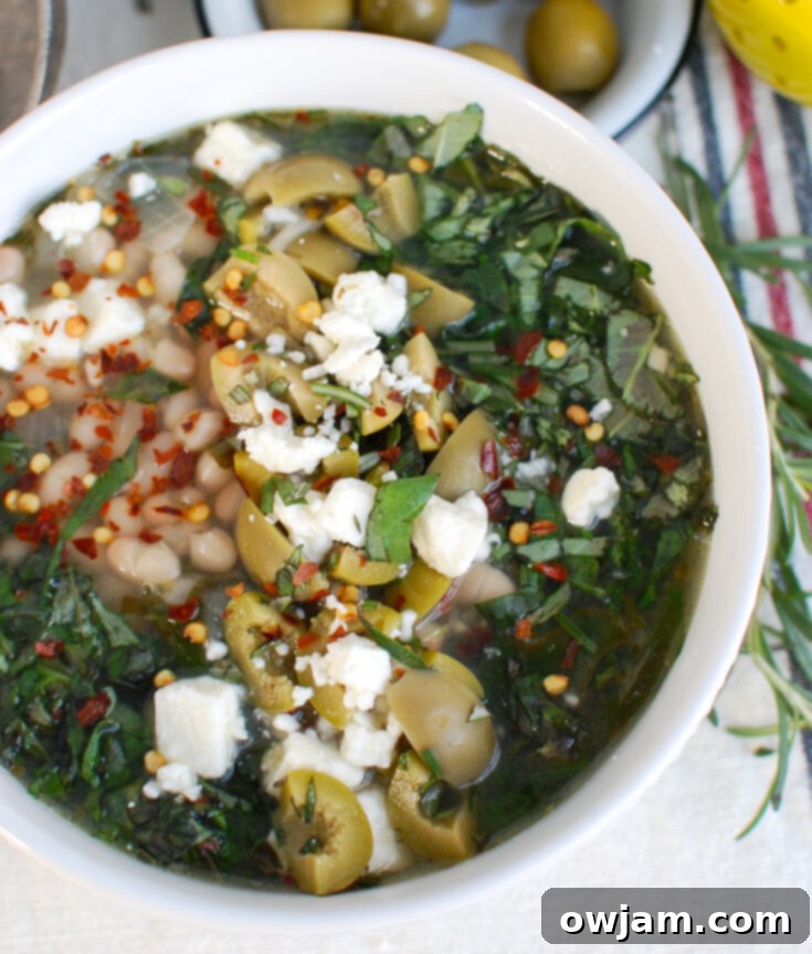 Hearty Navy Bean Soup with greens, crumbled feta, and black olives in a white bowl