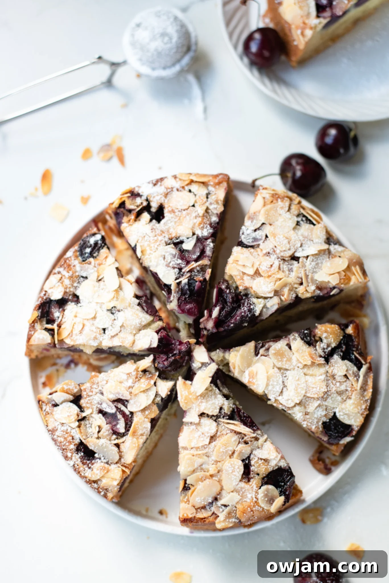 A beautifully presented whole Cherry Almond Cake, with a scattering of fresh cherries and almonds on a wooden board.
