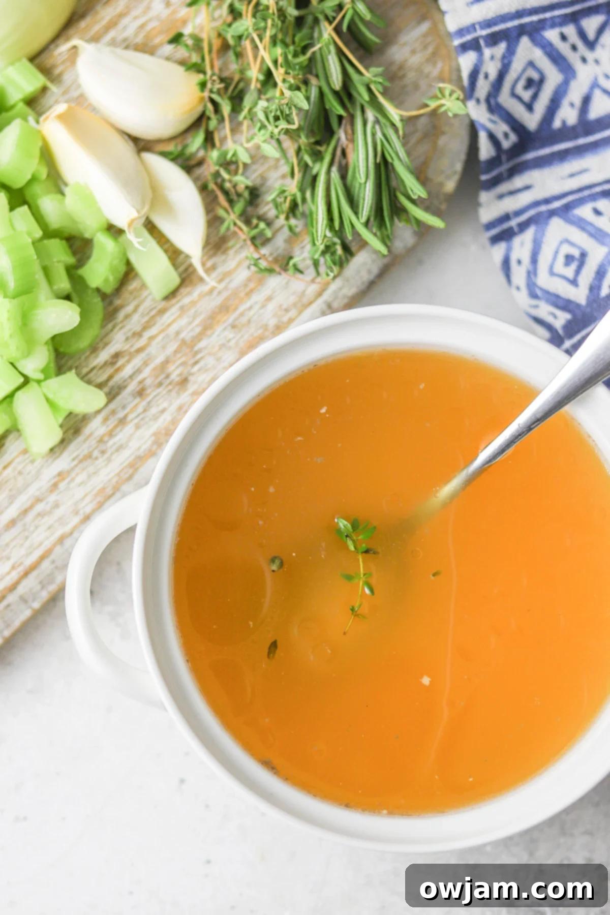 Slow-Simmered Chicken Broth 8 Homemade Chicken Broth in a white bowl with a ladle, garnished with fresh herbs.