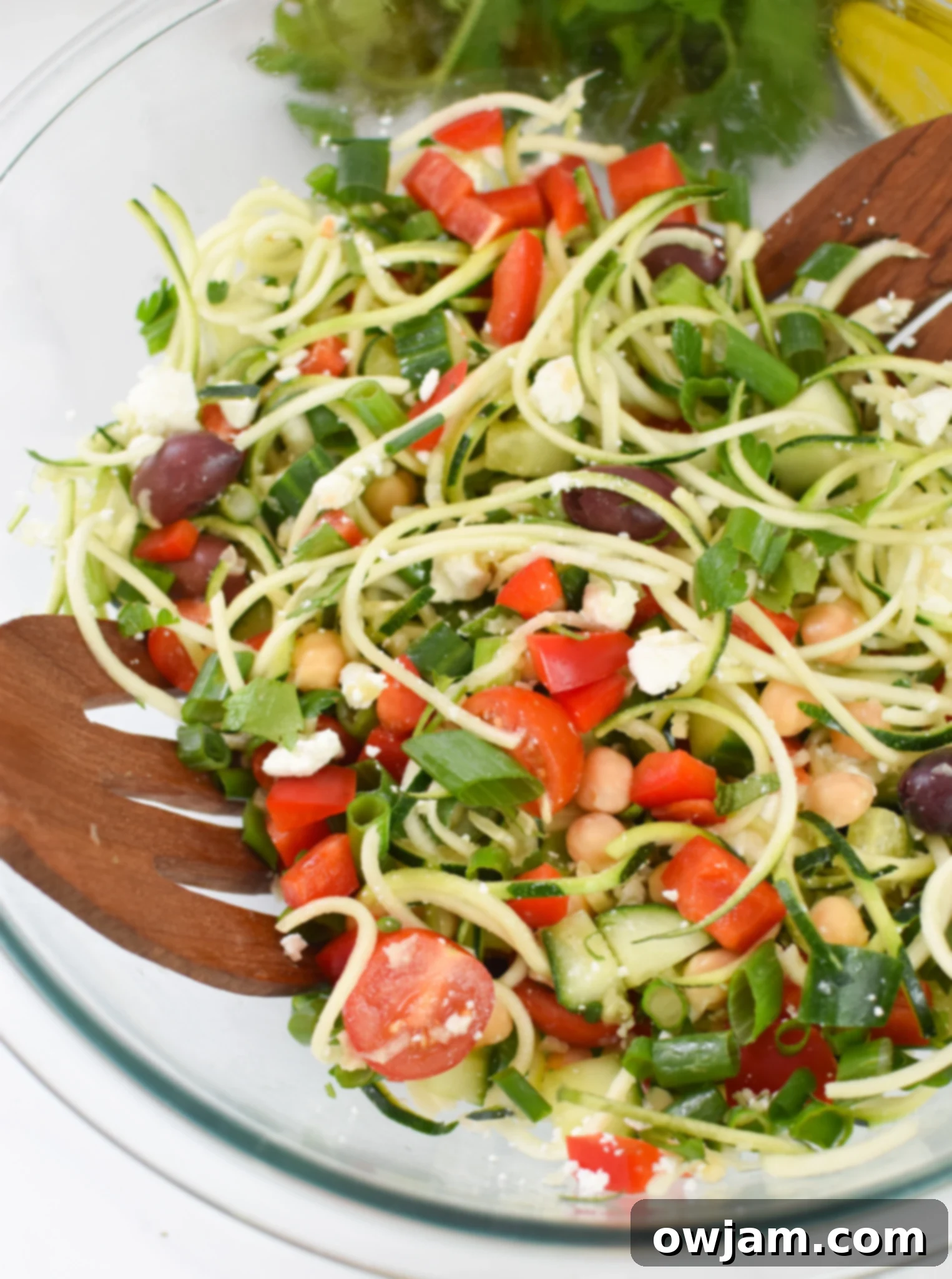 A vibrant Mediterranean Zucchini Pasta Salad served in a clear glass bowl, showcasing colorful vegetables and feta cheese, ready for a summer meal.