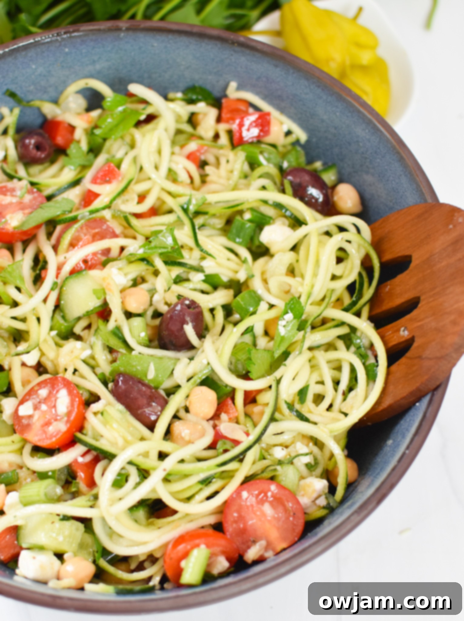 Sun-Kissed Zucchini Pasta Medley 5 A serving of Mediterranean Zucchini Pasta Salad in a blue bowl, garnished with fresh herbs and lemon, with wooden tongs for serving.