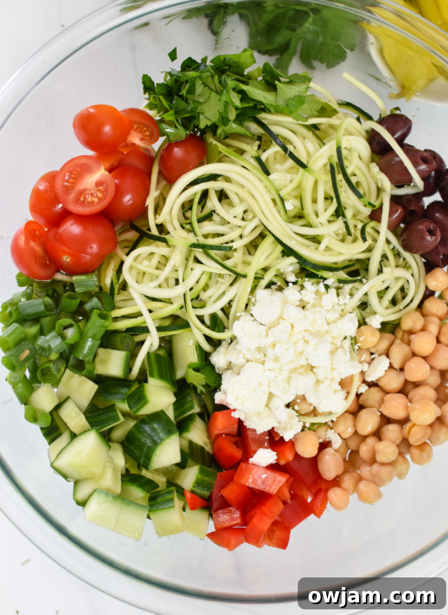 Sun-Kissed Zucchini Pasta Medley 7 Close-up of Mediterranean Zucchini Pasta Salad ingredients in a glass bowl, showcasing the vibrant colors and fresh textures before mixing.