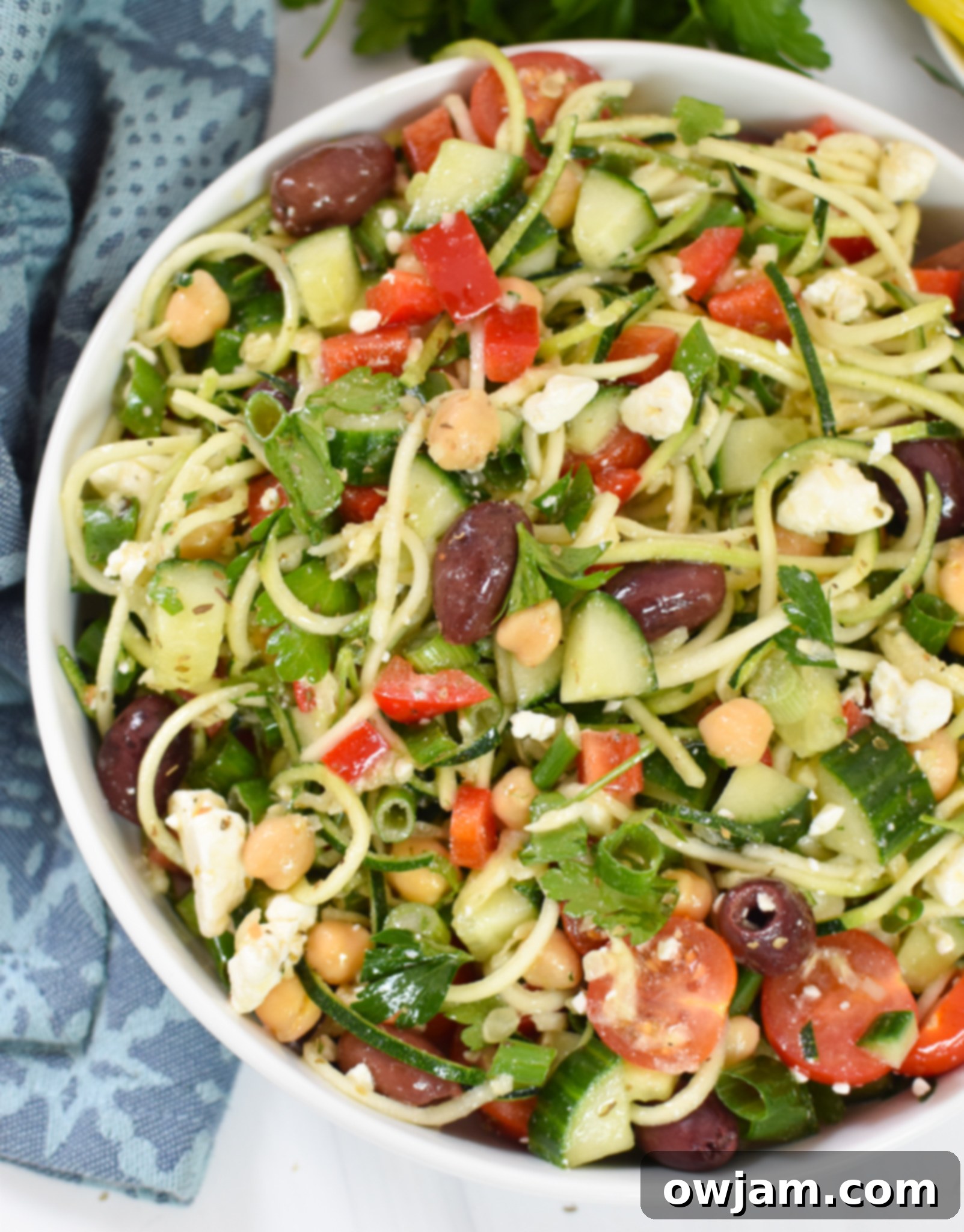 Sun-Kissed Zucchini Pasta Medley 8 A large glass bowl filled with Mediterranean Zucchini Pasta Salad, with wooden tongs resting on the rim, ready to be served.
