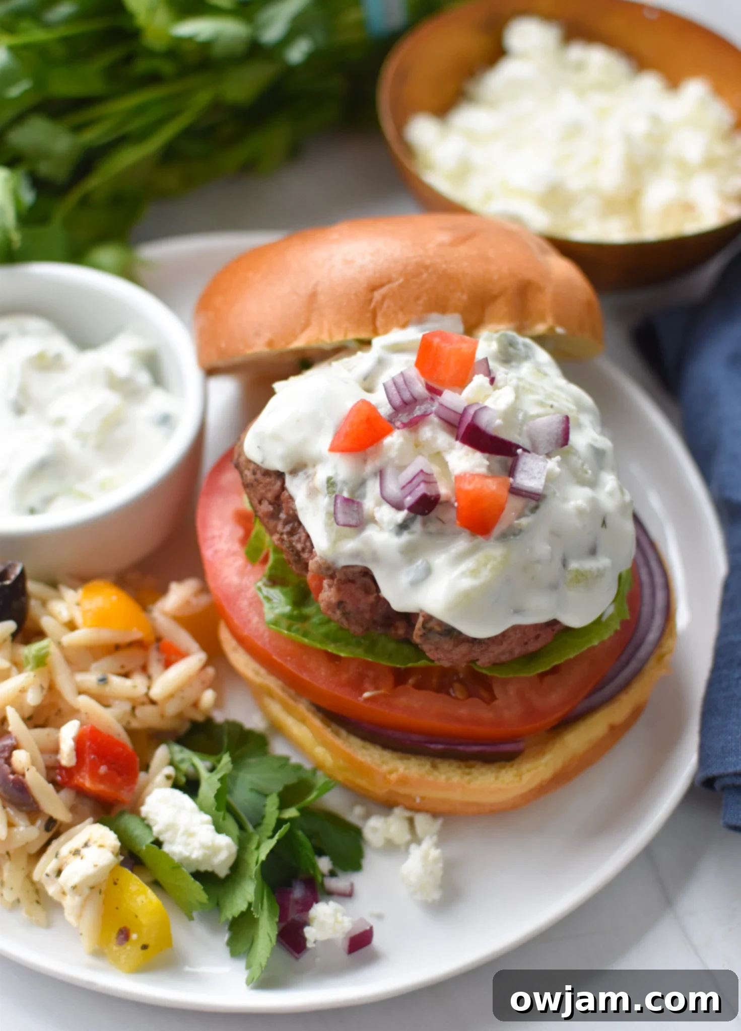 Juicy Feta Burger with a generous dollop of creamy tzatziki sauce, served on a bun with fresh toppings.
