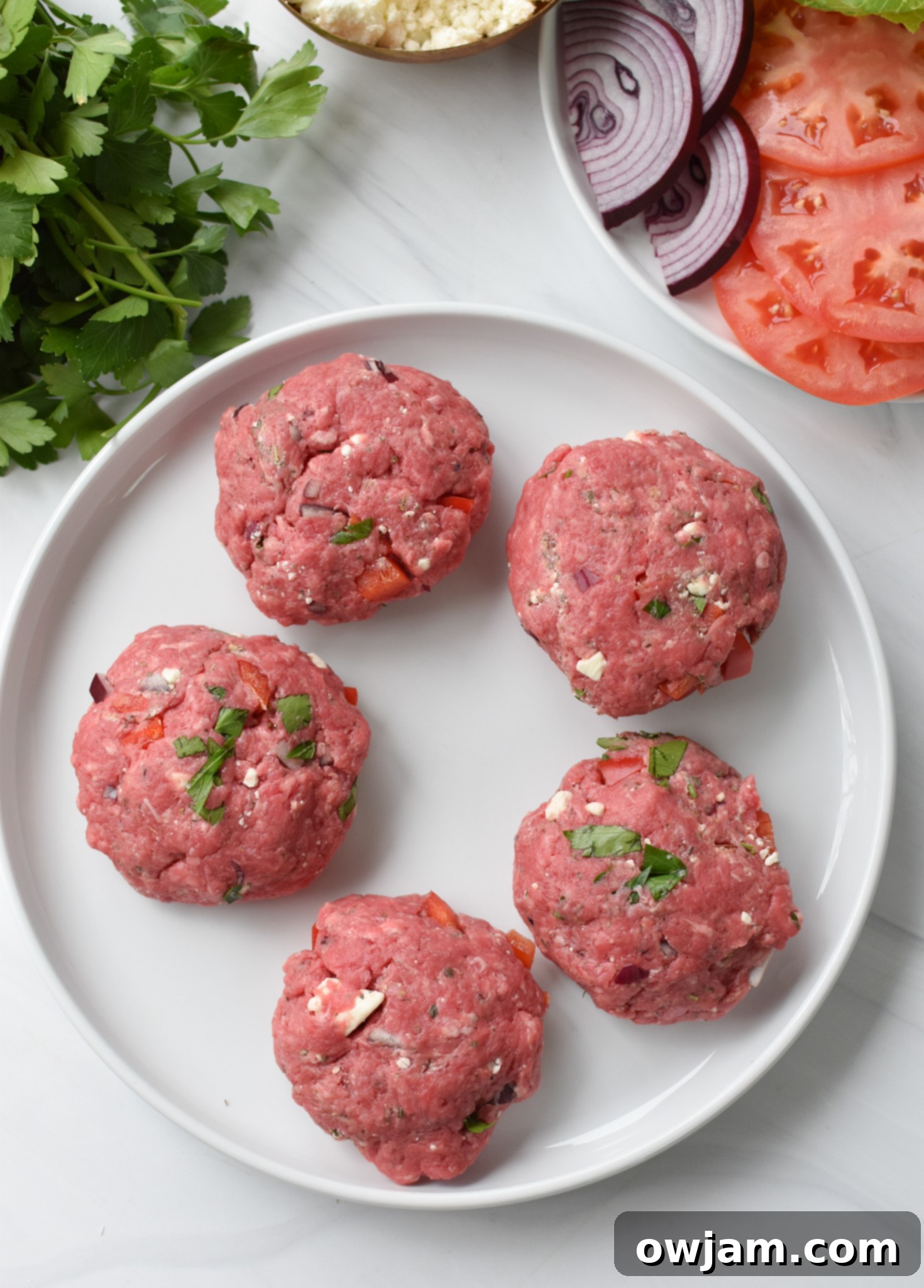 Four perfectly formed Feta Burger patties on a white plate, ready for cooking.