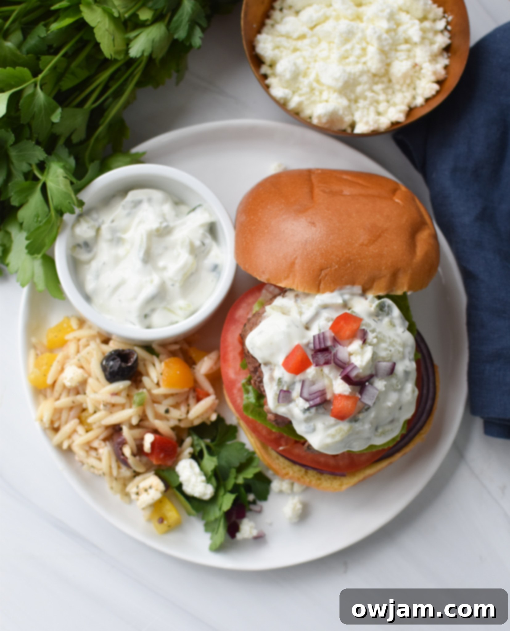 A vibrant Feta Burger with Tzatziki, garnished with fresh herbs and bell peppers, on a plate.