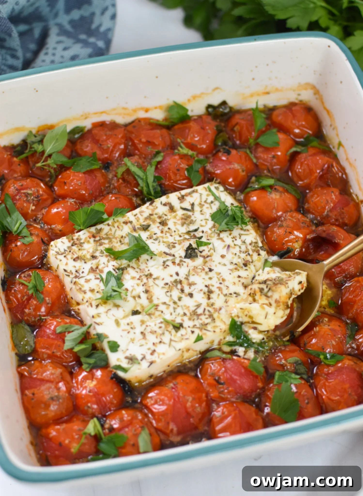 Simple Baked Feta Perfection 4 Easy Baked Feta Recipe served warm in a blue baking dish with a golden serving spoon, garnished with fresh herbs.