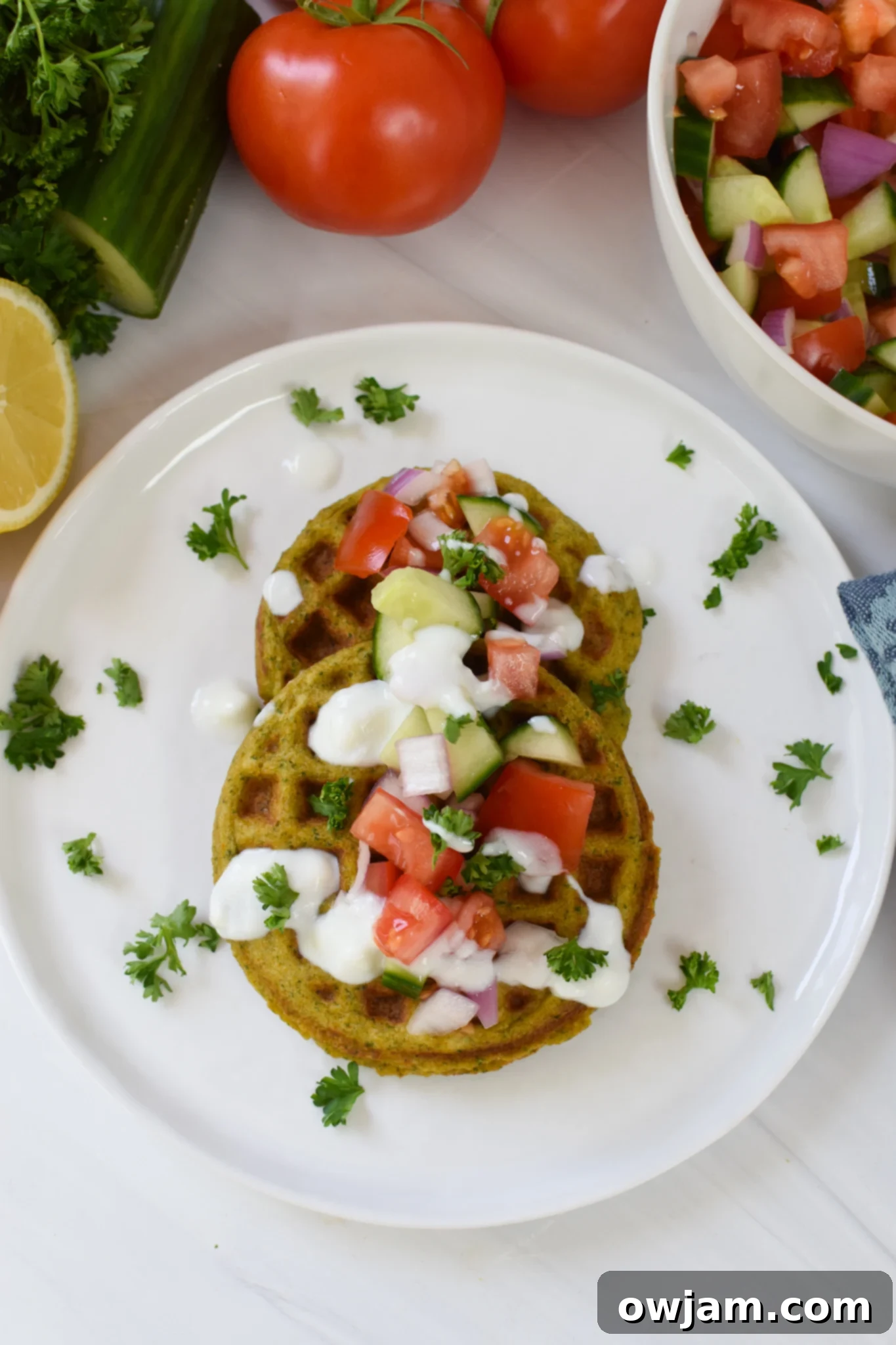 Crispy Falafel Waffles topped with fresh Lebanese salad and tahini sauce, served on a white plate, perfect for a Mediterranean breakfast.