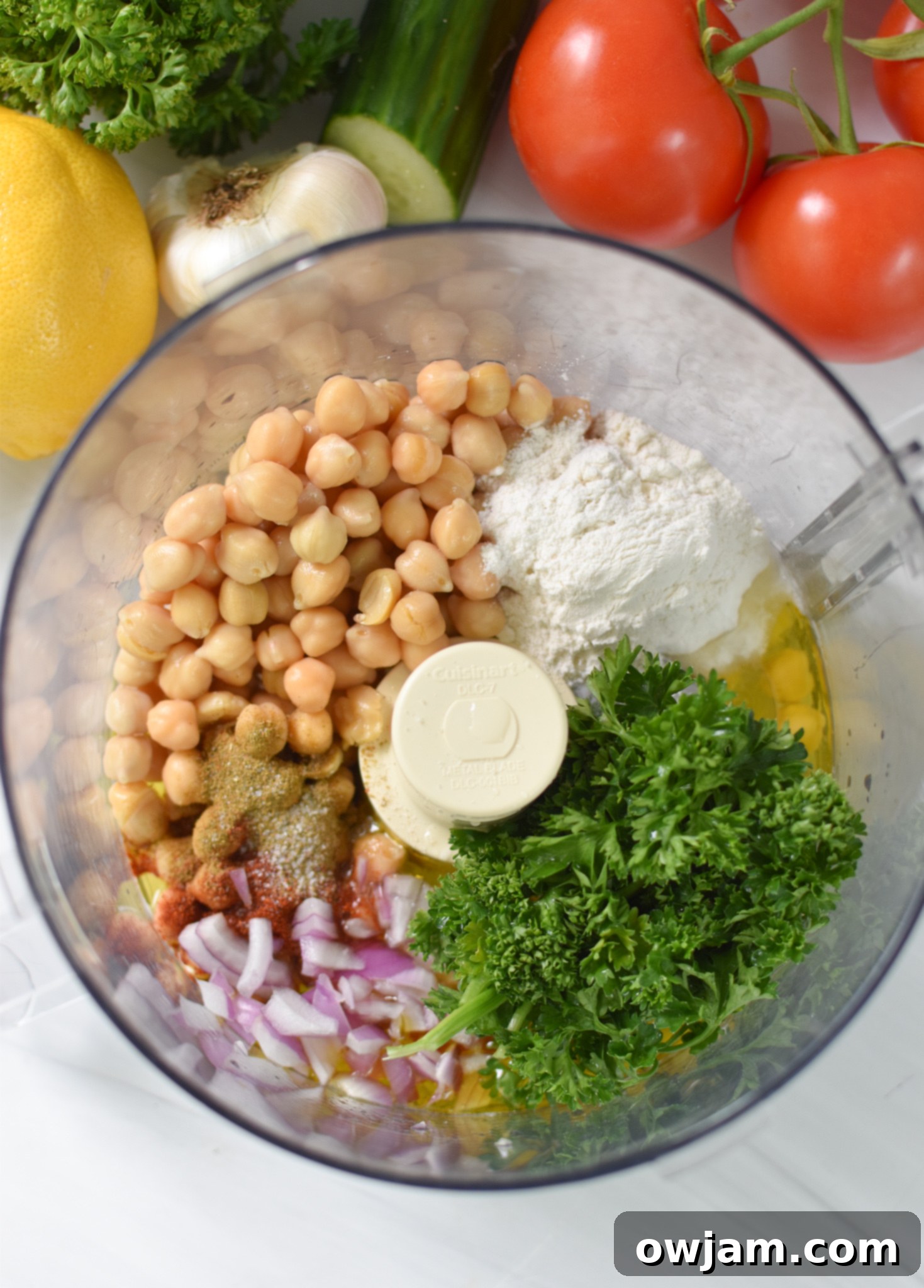Chickpea mixture with red onion, parsley, and spices in a food processor, ready to be blended into falafel waffle batter.