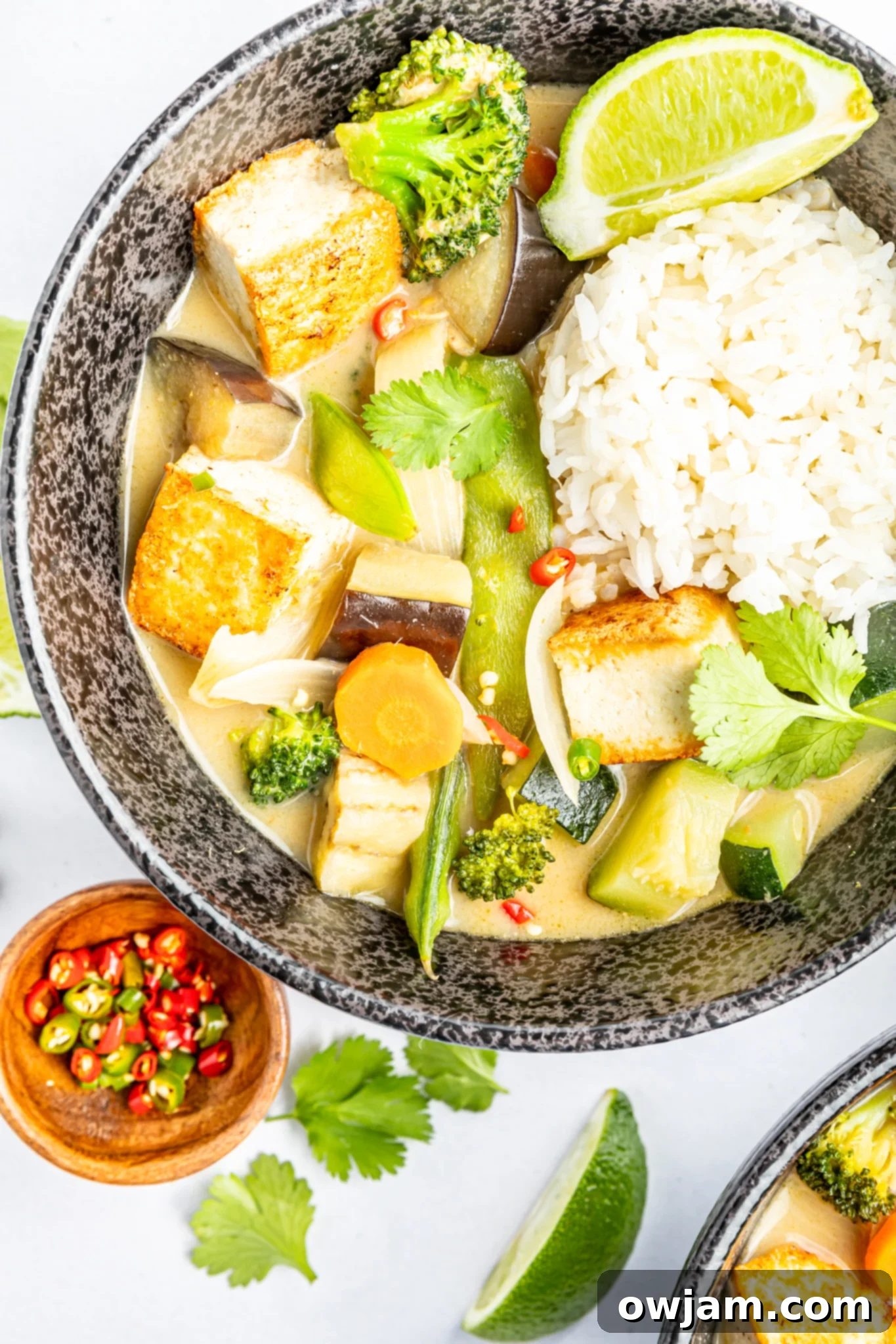 A bowl of vibrant Thai Vegetable Green Curry, garnished with fresh cilantro and crushed peanuts, served with steamed rice on the side.