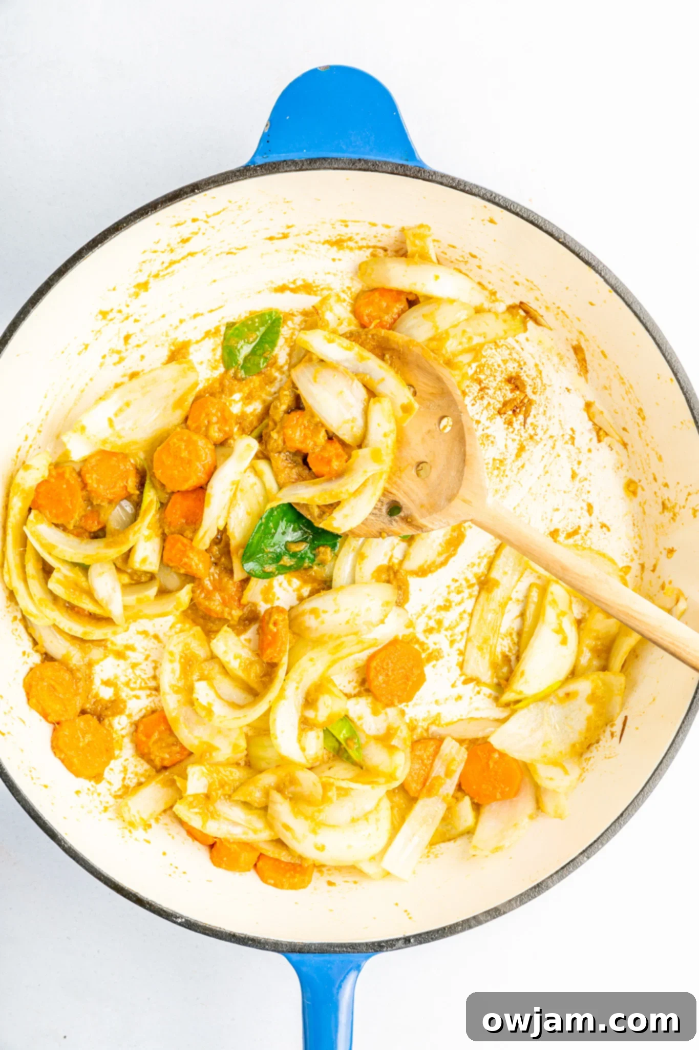 Onions, garlic, and carrots sautéing in a skillet, forming the aromatic base for the green curry.