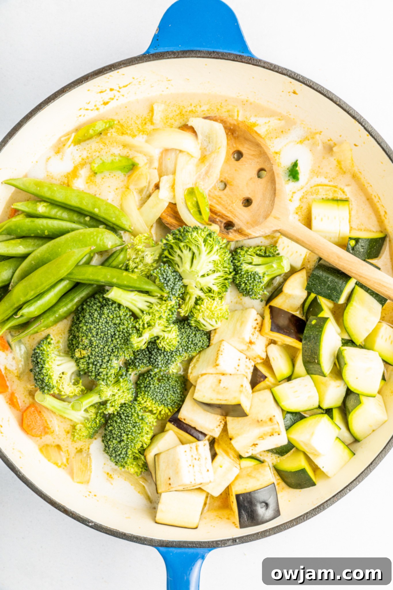 Green curry paste and lime leaves simmering in a pot with vegetables, creating a rich and fragrant base.