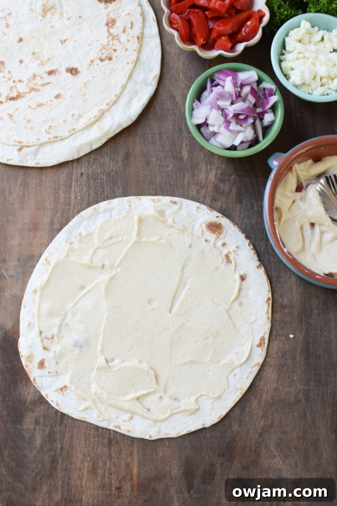 Savory Mediterranean Spirals 5 A tortilla with a layer of hummus spread evenly across its surface, ready for filling.