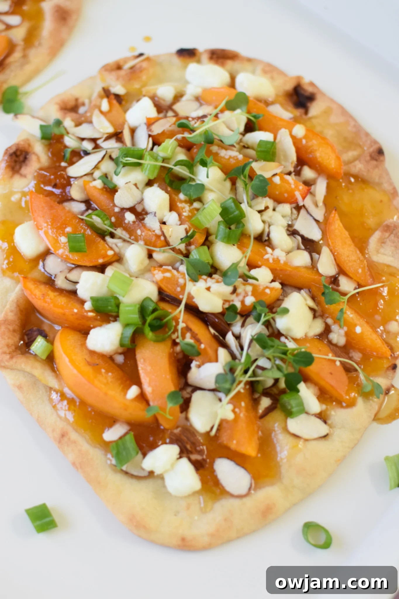 Goat Cheese Apricot Pizza on a white plate, garnished with fresh green onions and micro-greens.