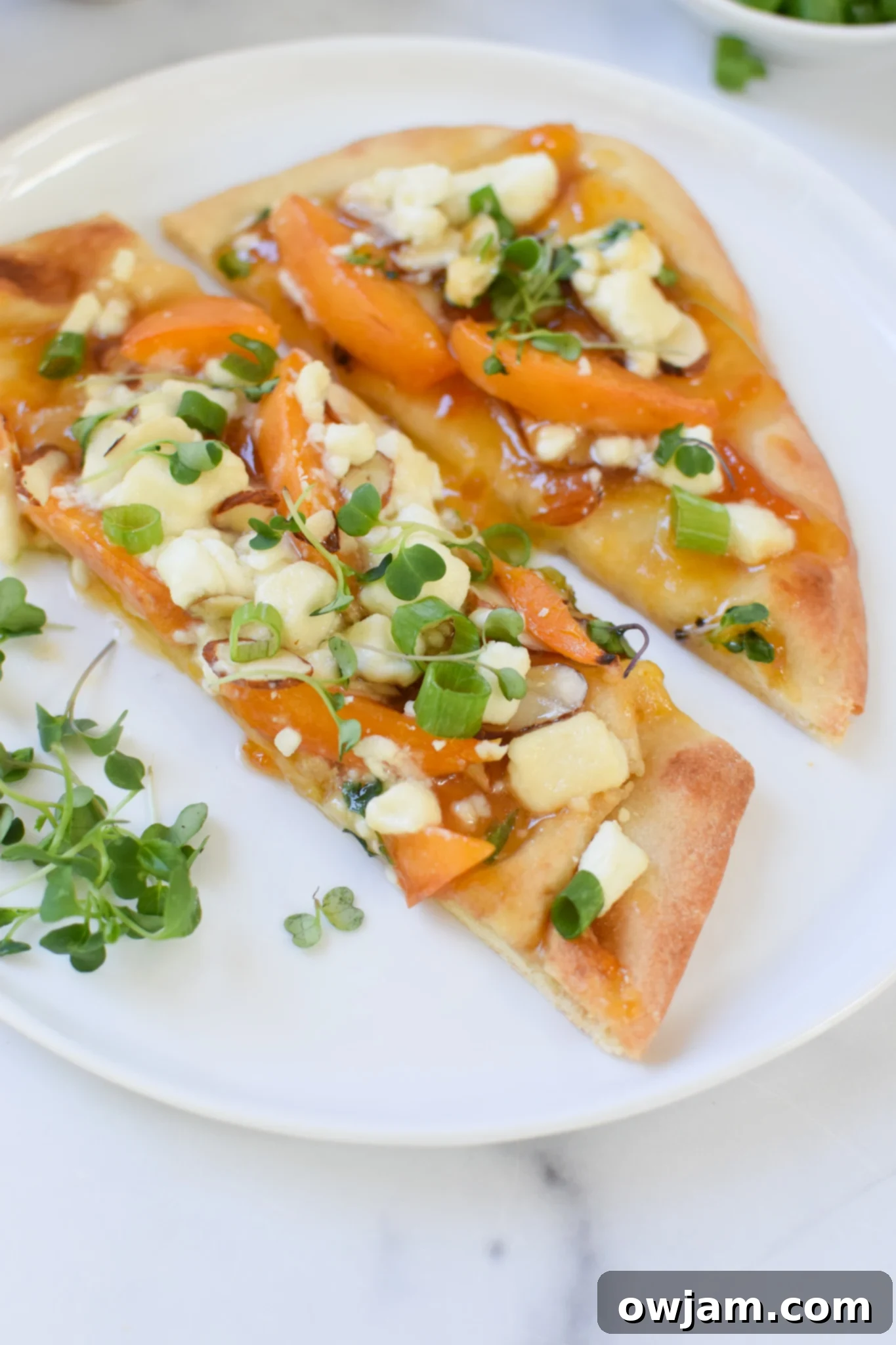 Goat Cheese Apricot Pizza sliced into wedges on a white serving plate, with a fork next to it.