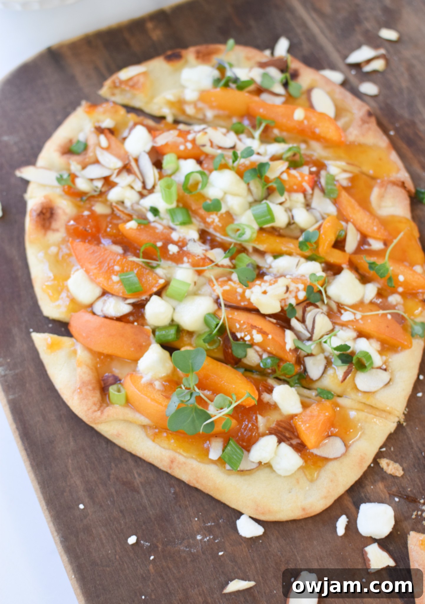 Close-up of Goat Cheese Apricot Pizza slices, showing the melted cheese, caramelized apricots, and green garnishes.