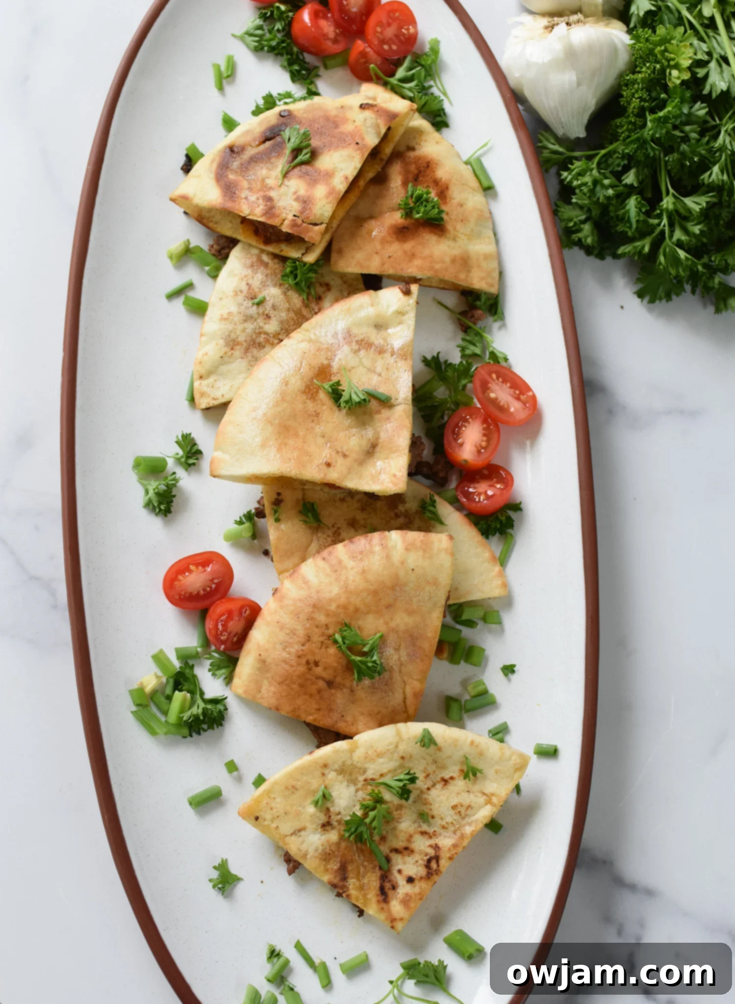 Arayes Lebanese Grilled Meat Stuffed Pitas 5 A close-up of a Lebanese Meat Stuffed Pita, still warm and golden, garnished with fresh diced tomatoes and finely chopped parsley, ready for a delicious bite.