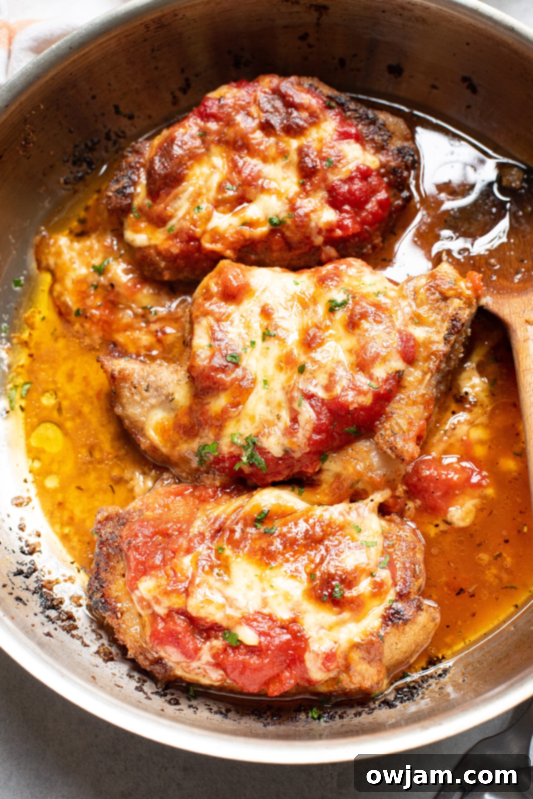 Golden Parmesan Pork Chops 4 A Parmesan Crusted Pork Chop resting in a skillet, topped with marinara sauce and shredded mozzarella cheese.