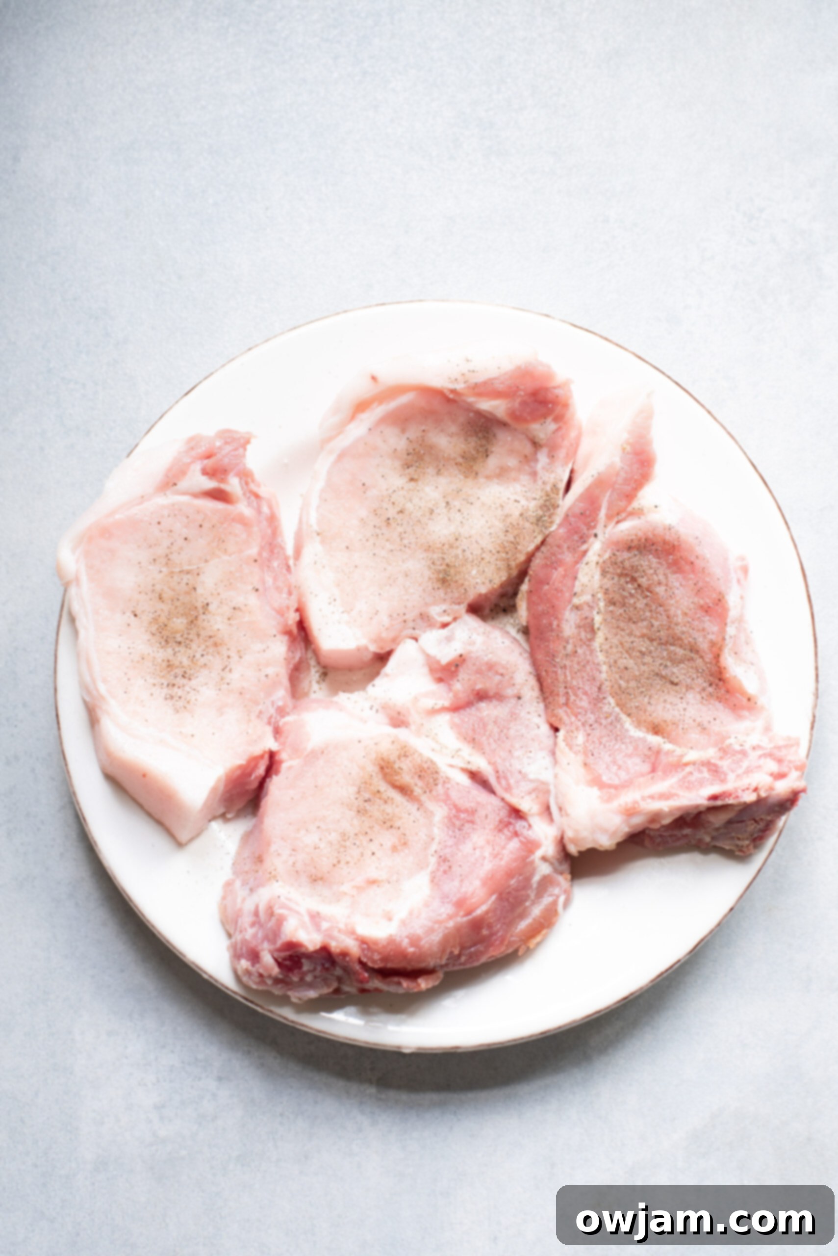 Golden Parmesan Pork Chops 5 A raw pork chop being pressed into a mixture of breadcrumbs and Parmesan cheese.