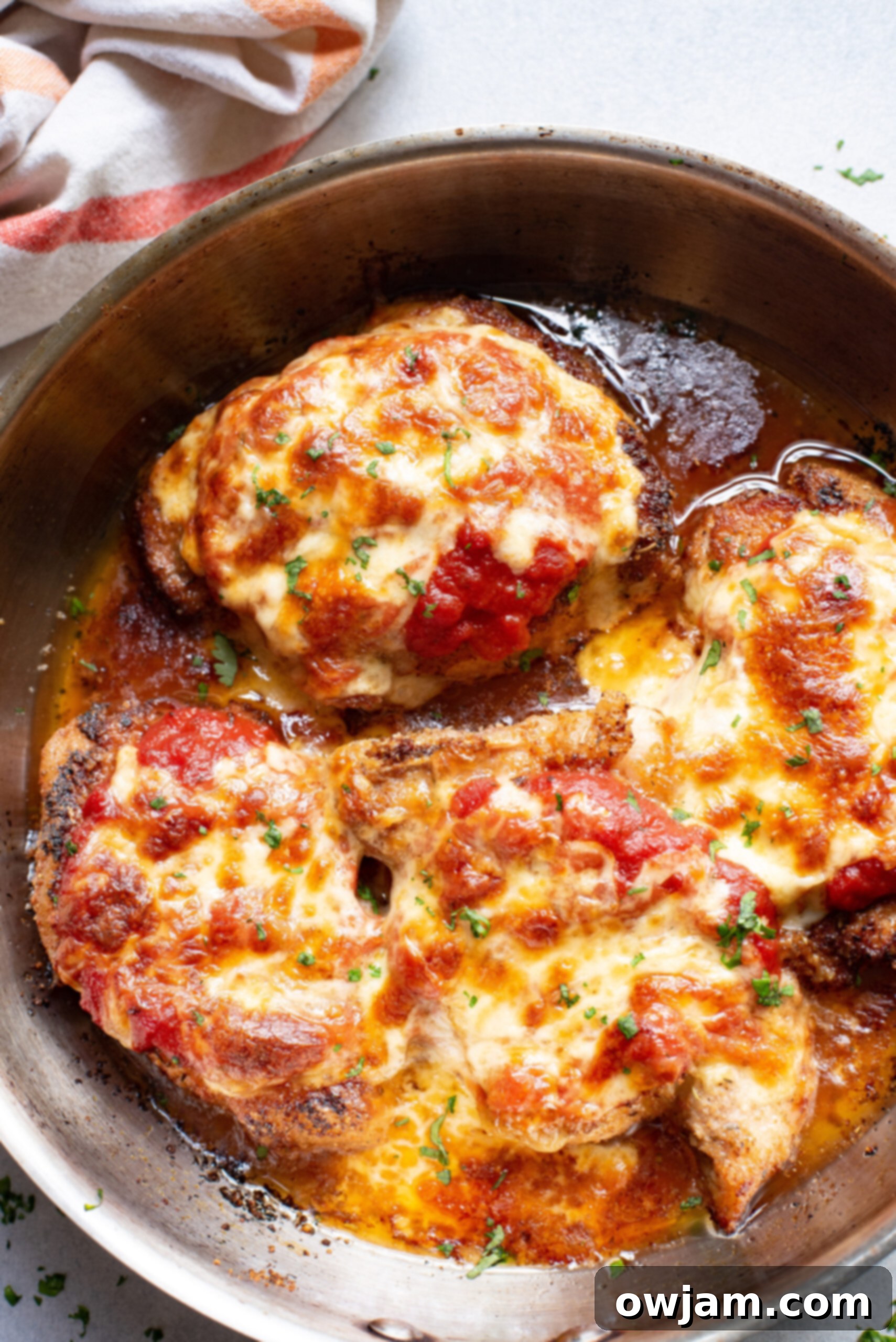 Golden Parmesan Pork Chops 9 Close-up of baked Parmesan Crusted Pork Chops with melted cheese and sauce, garnished with fresh herbs.
