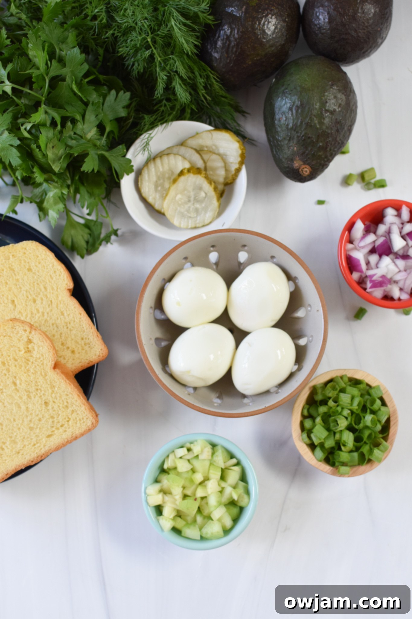 Creamy Avocado Egg Salad 3 Fresh ingredients for Avocado Egg Salad laid out, including hard-boiled eggs, ripe avocado, dill, parsley, and onions.