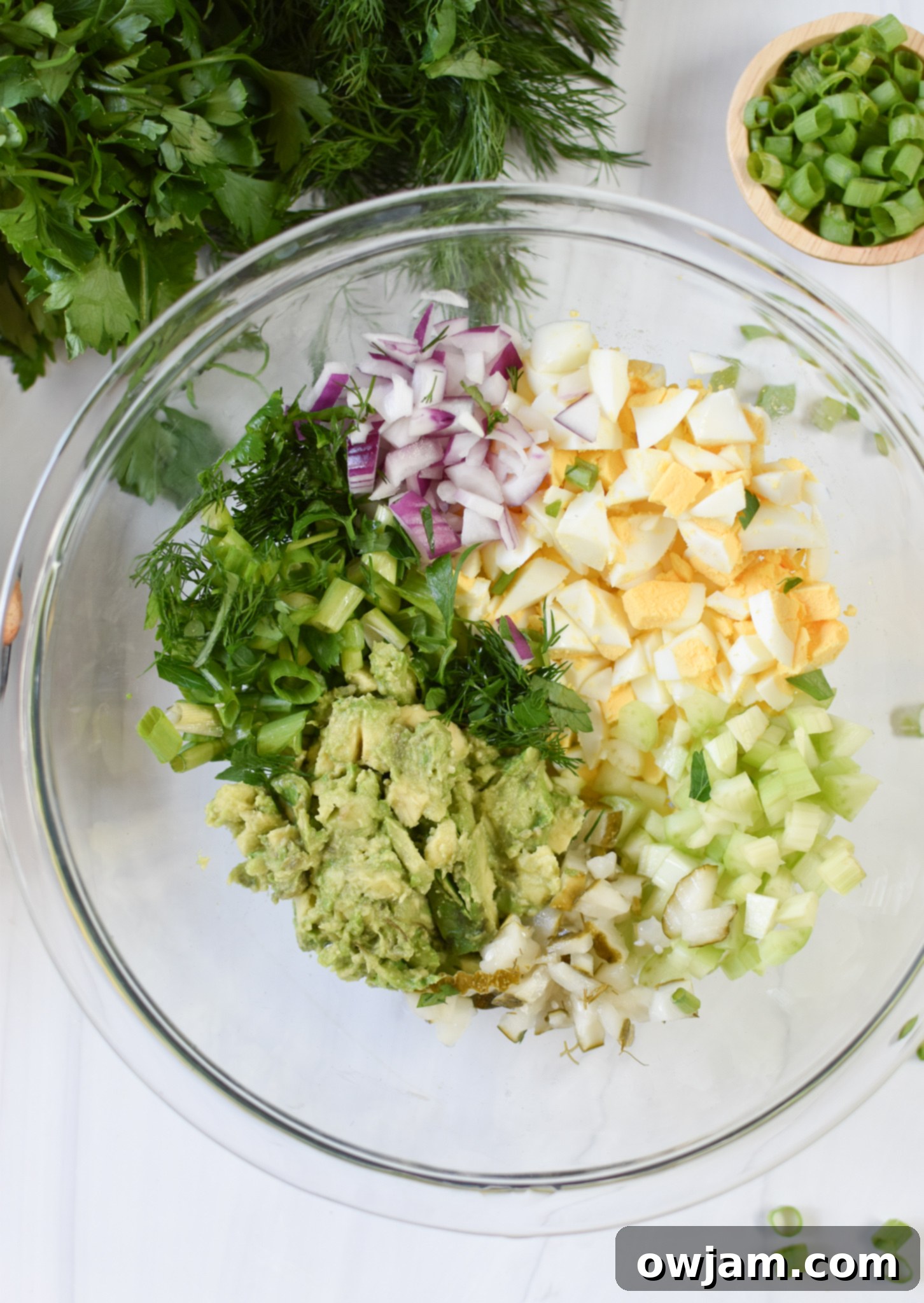Creamy Avocado Egg Salad 5 Mashed avocado, chopped pickles, and fresh vegetables in a mixing bowl, ready for egg salad.