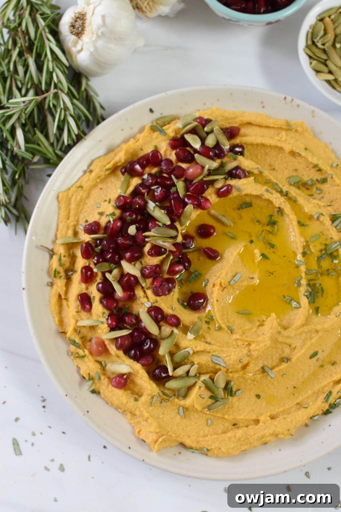 Velvet Pumpkin Dip 2 Creamy Pumpkin Hummus garnished with pumpkin seeds and a sprig of rosemary, ready to be served.